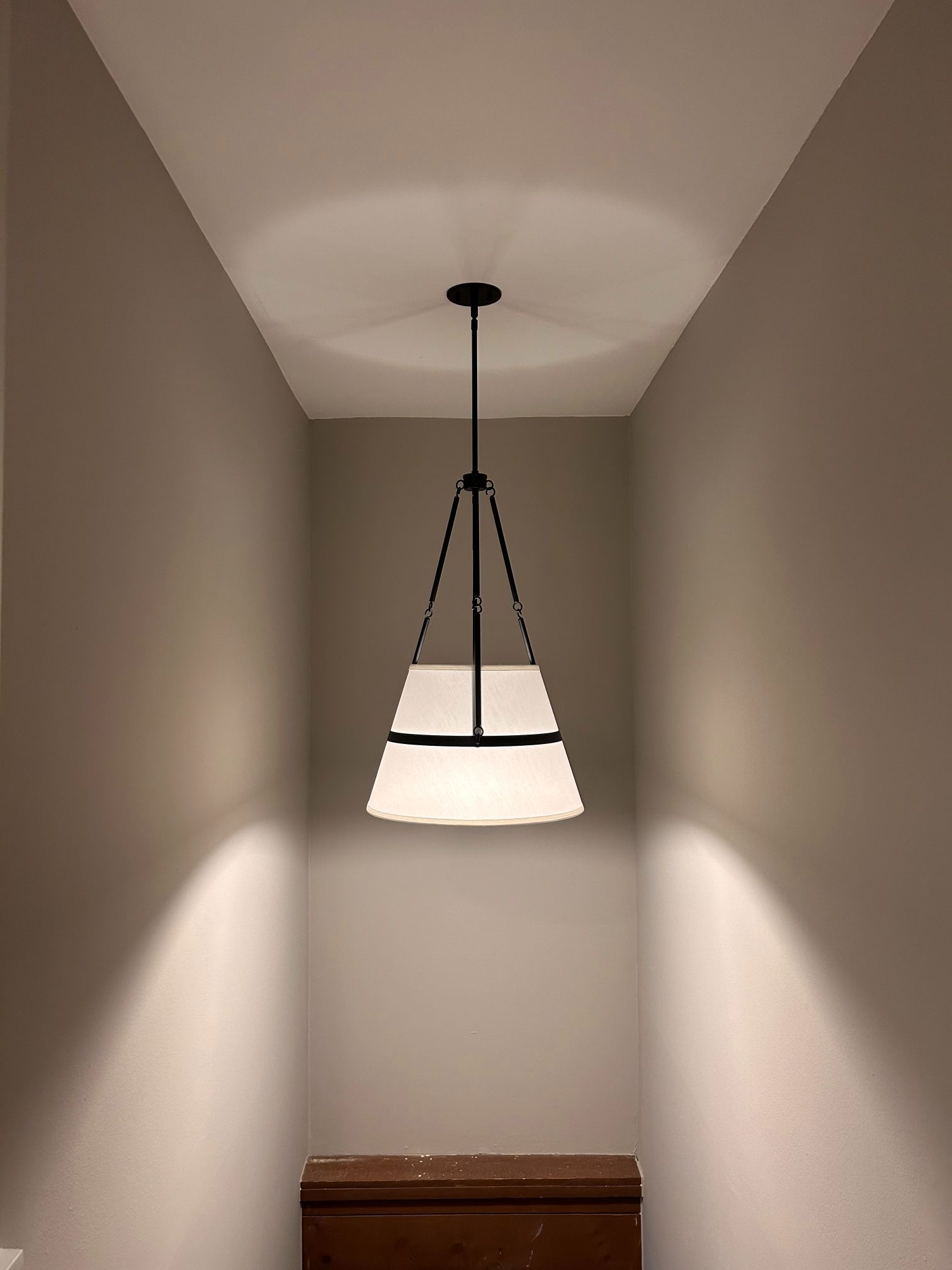 Hanging pendant light in a narrow hallway casting soft light on beige walls.
