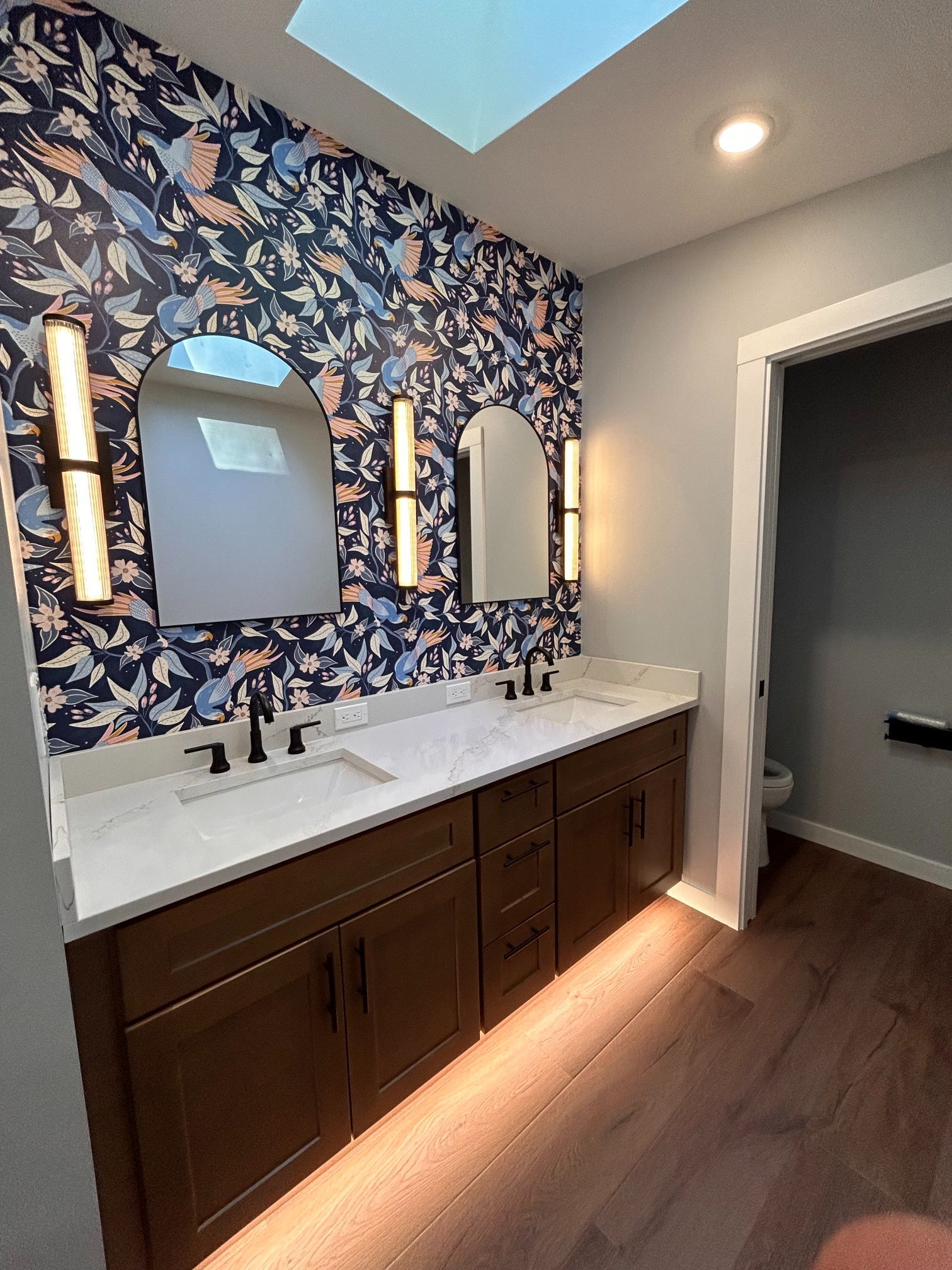 Modern bathroom vanity with blue floral wallpaper, double mirrors, and dark wood cabinets