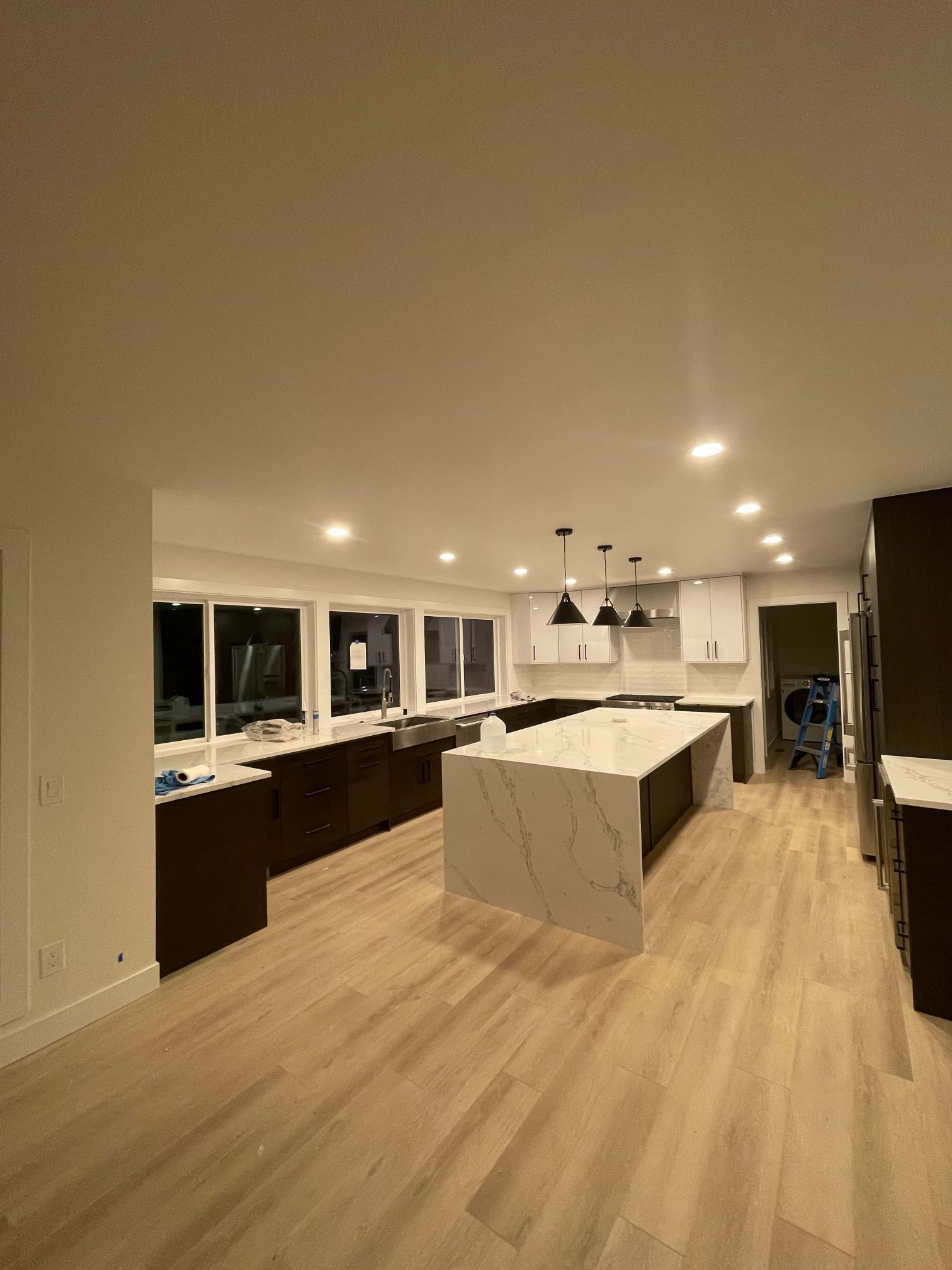 Modern open kitchen with island, wood floors, white cabinets, and pendant lights at night
