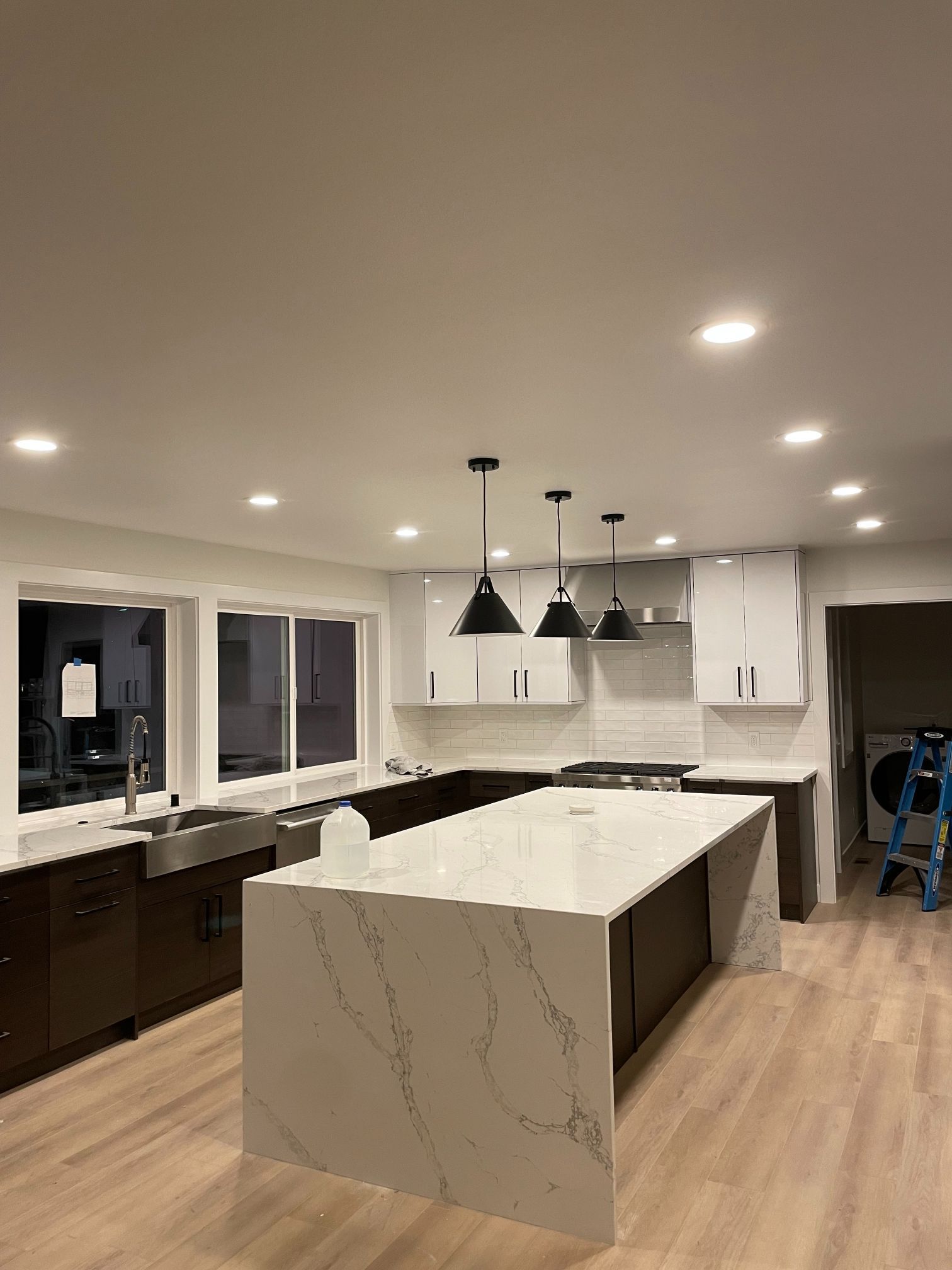 Modern kitchen with white marble island, dark lower cabinets, pendant lights, and recessed ceiling lights.