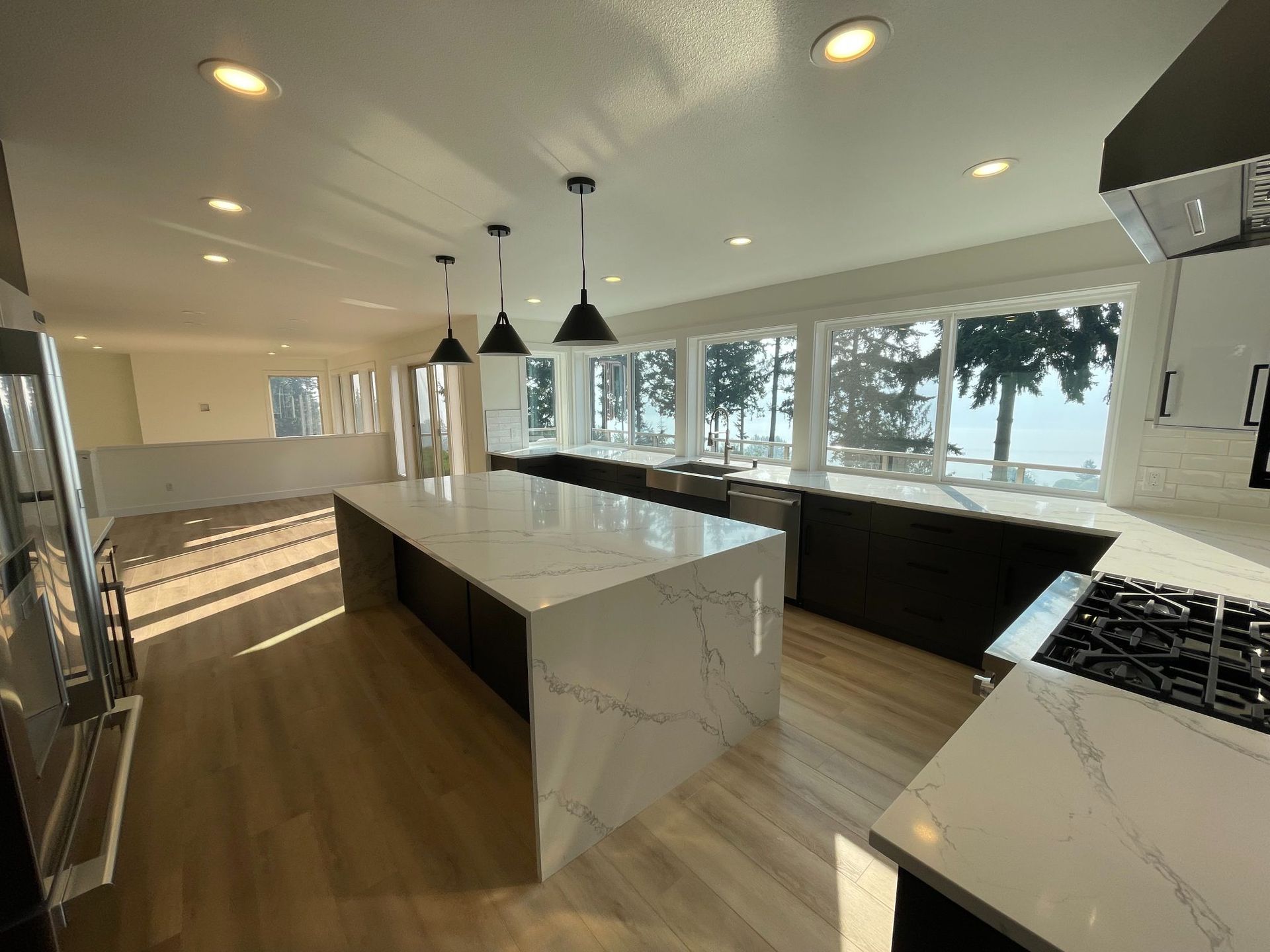 Modern kitchen with marble island, black pendants, and large windows overlooking trees