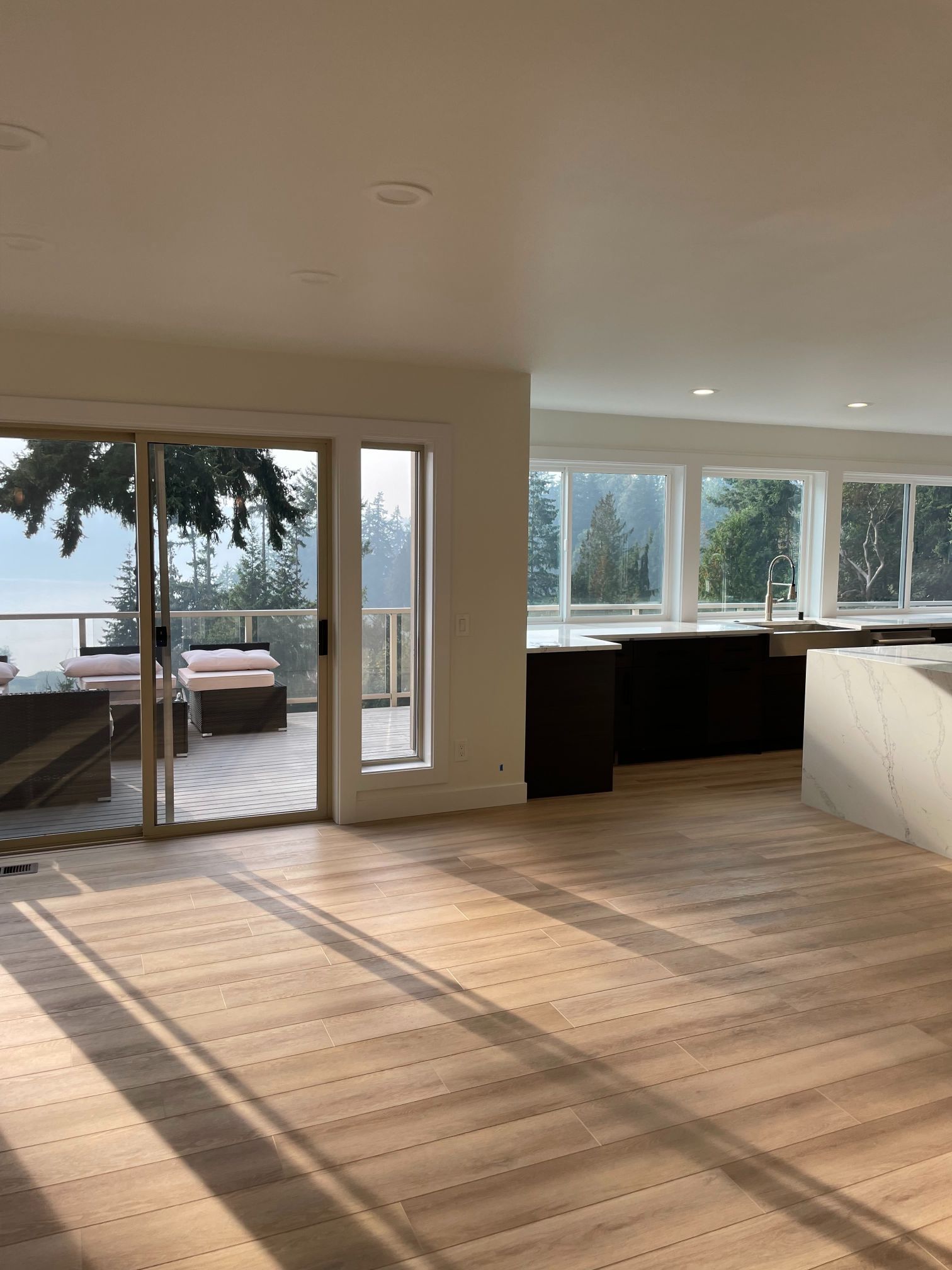 Spacious modern living room with large windows, sliding glass doors, and sunset light on the wood floor.