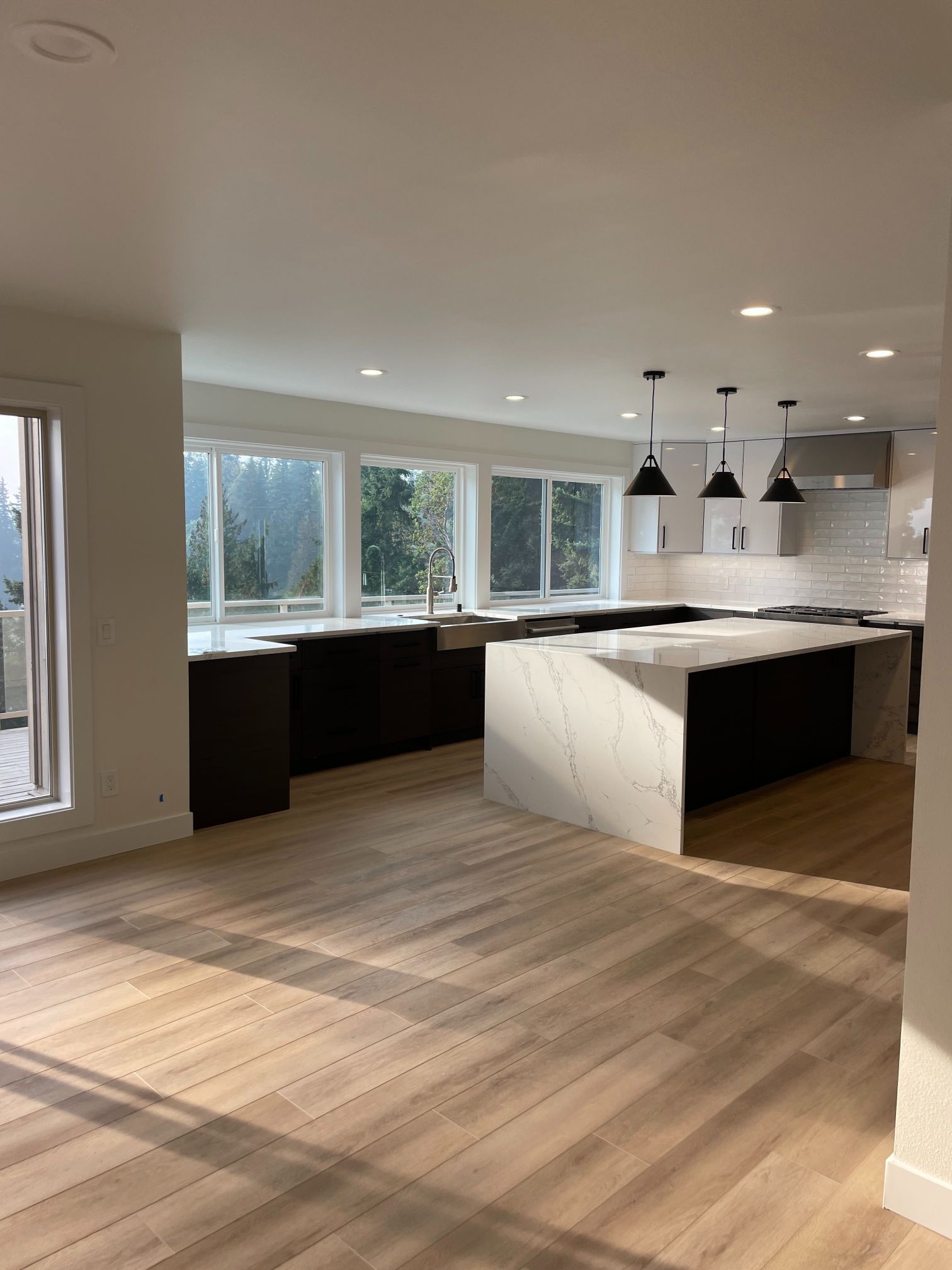 Bright modern kitchen with white island, dark cabinets, pendant lights, and large windows
