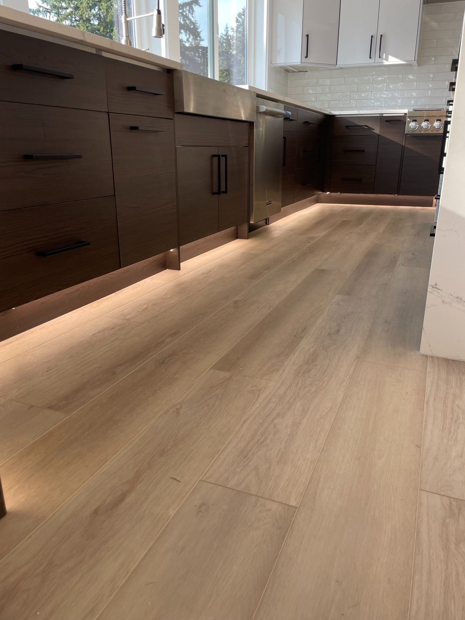 Modern kitchen with light wood flooring, dark cabinets, and natural light from windows