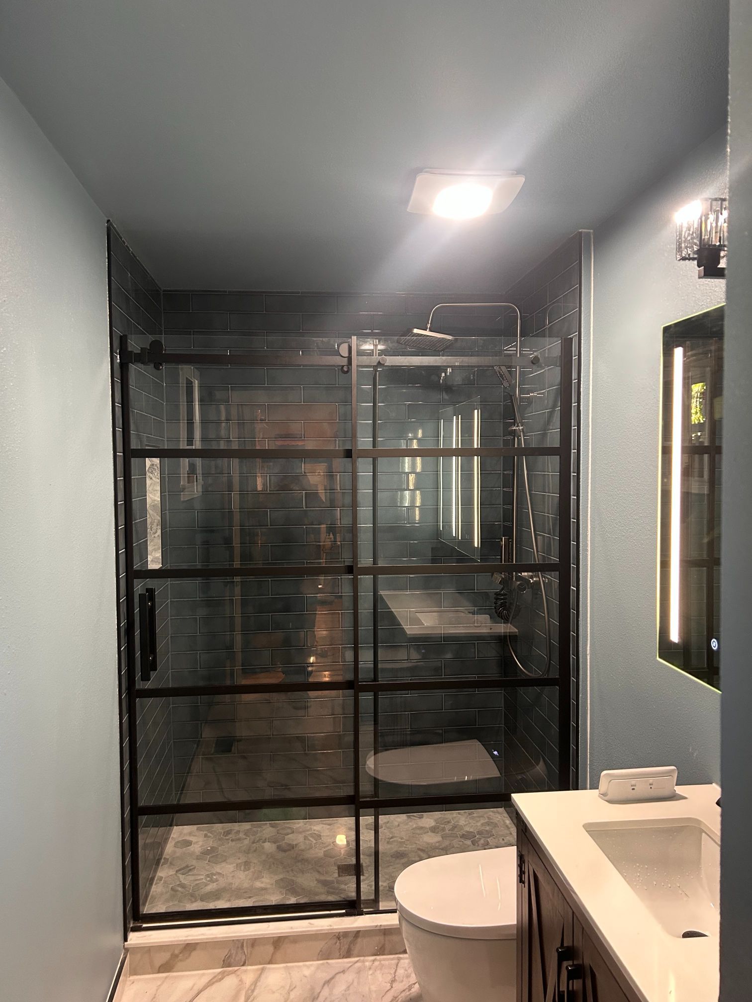 Modern bathroom with glass shower enclosure, white sink, and toilet in a dark-toned interior