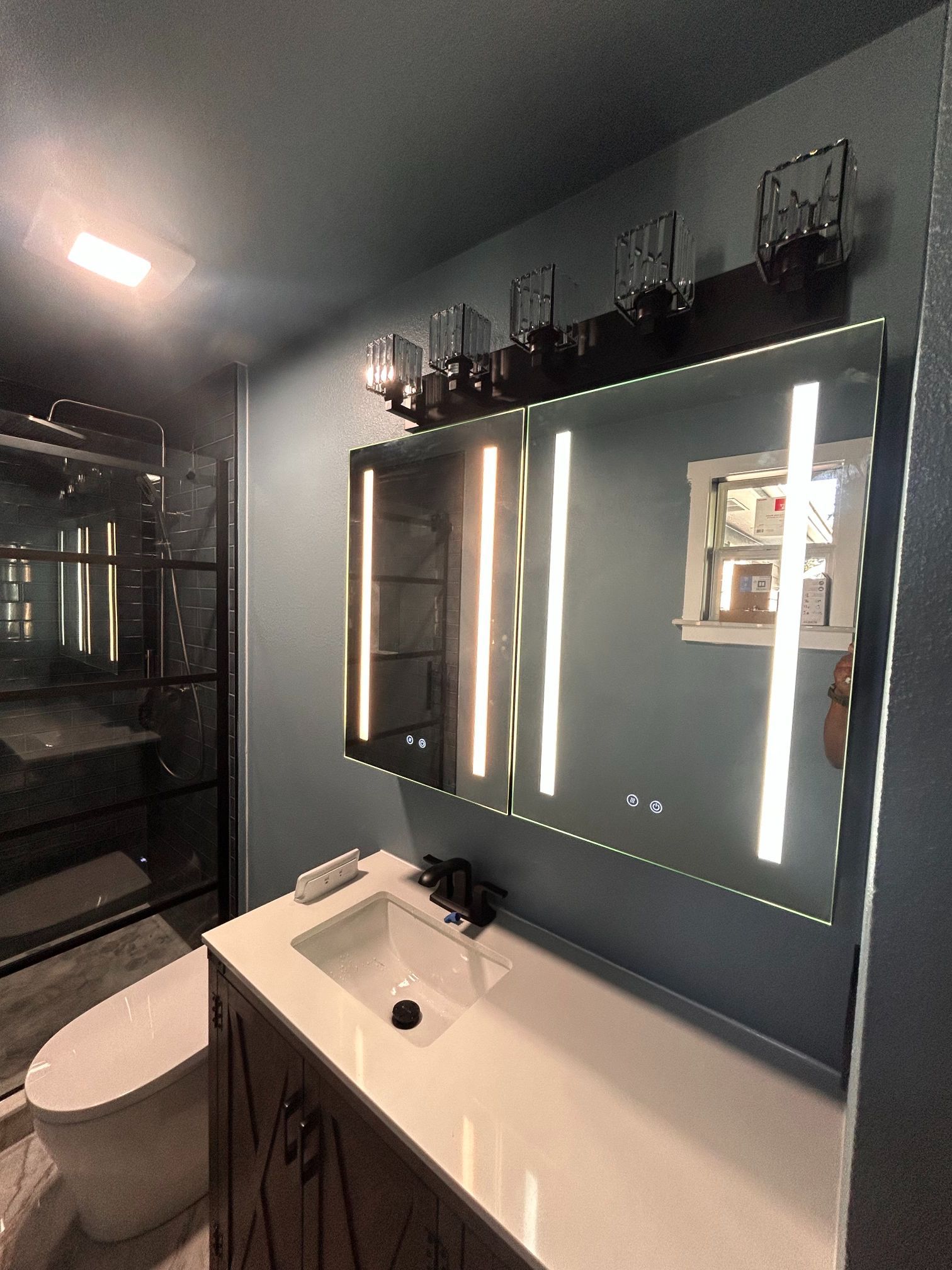 Modern bathroom with a large mirror, white vanity, and dark gray walls, viewed from the toilet area