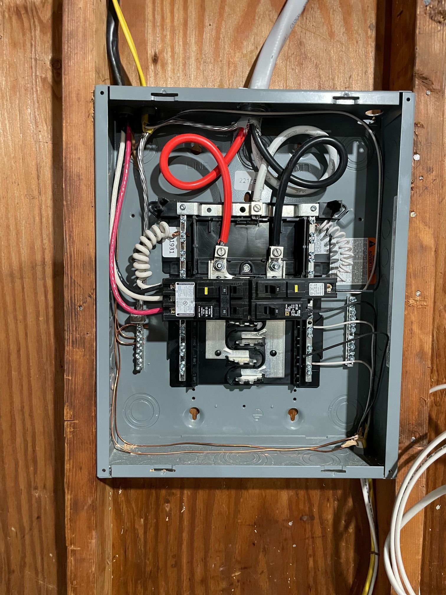 Open electrical breaker panel with wires and switches mounted on a wooden wall