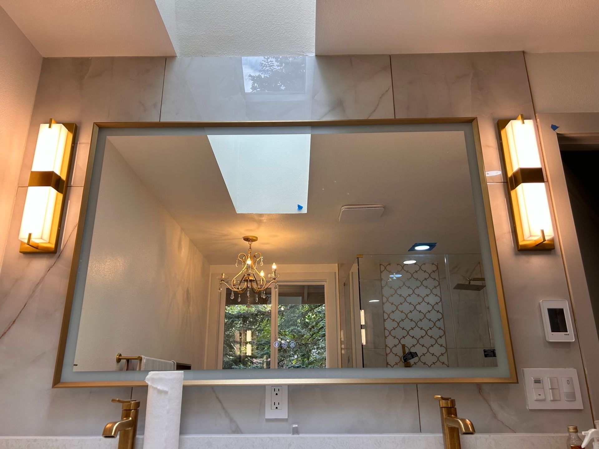 Bathroom vanity with large gold-framed mirror, wall sconces, and white countertop sink above brass fixtures.