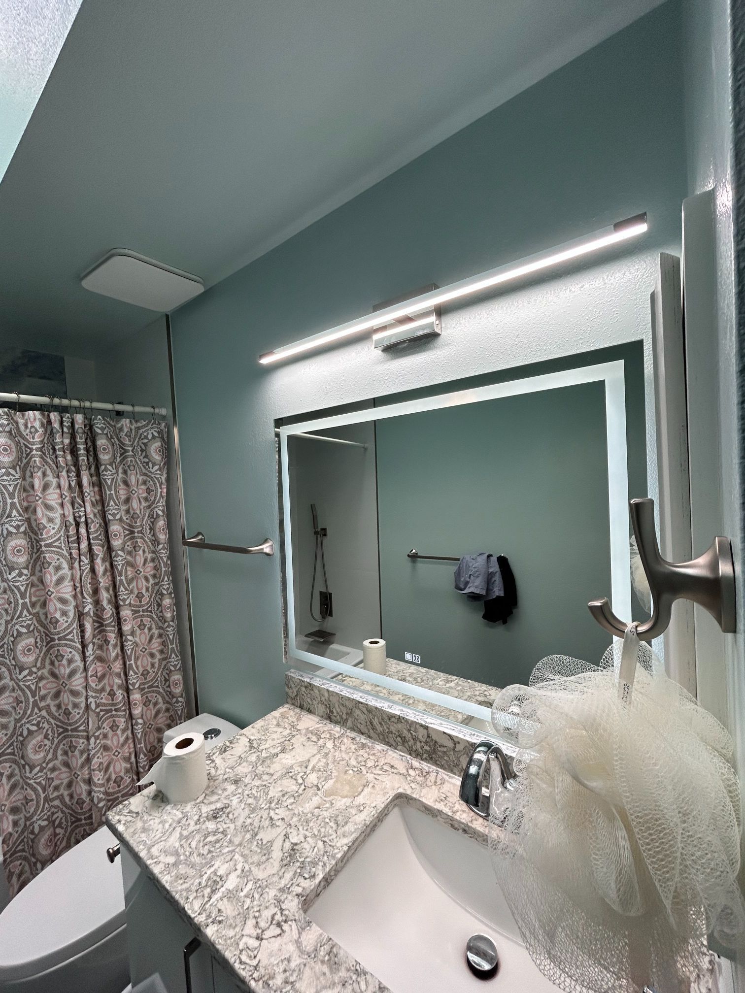Modern bathroom with a granite vanity, large mirror, wall light, and shower curtain on the left