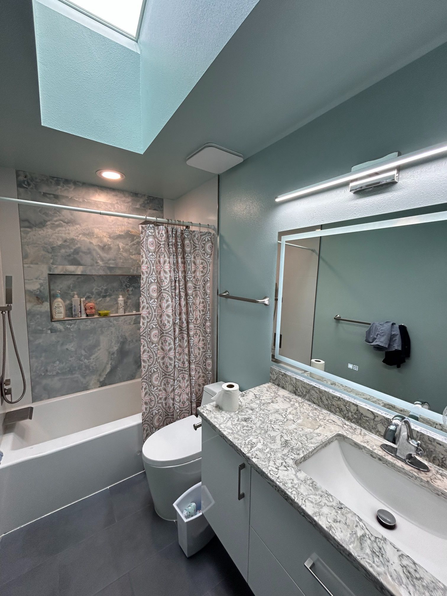 Modern bathroom with blue-green walls, white vanity and sink, large mirror, tub, and shower curtain