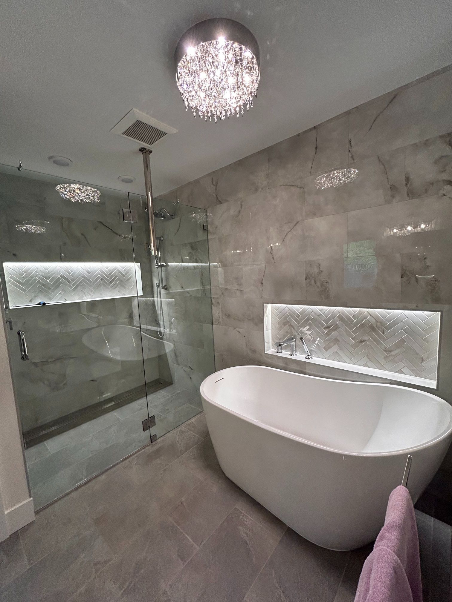 Modern gray bathroom with glass shower, freestanding tub, and illuminated mirror shelves