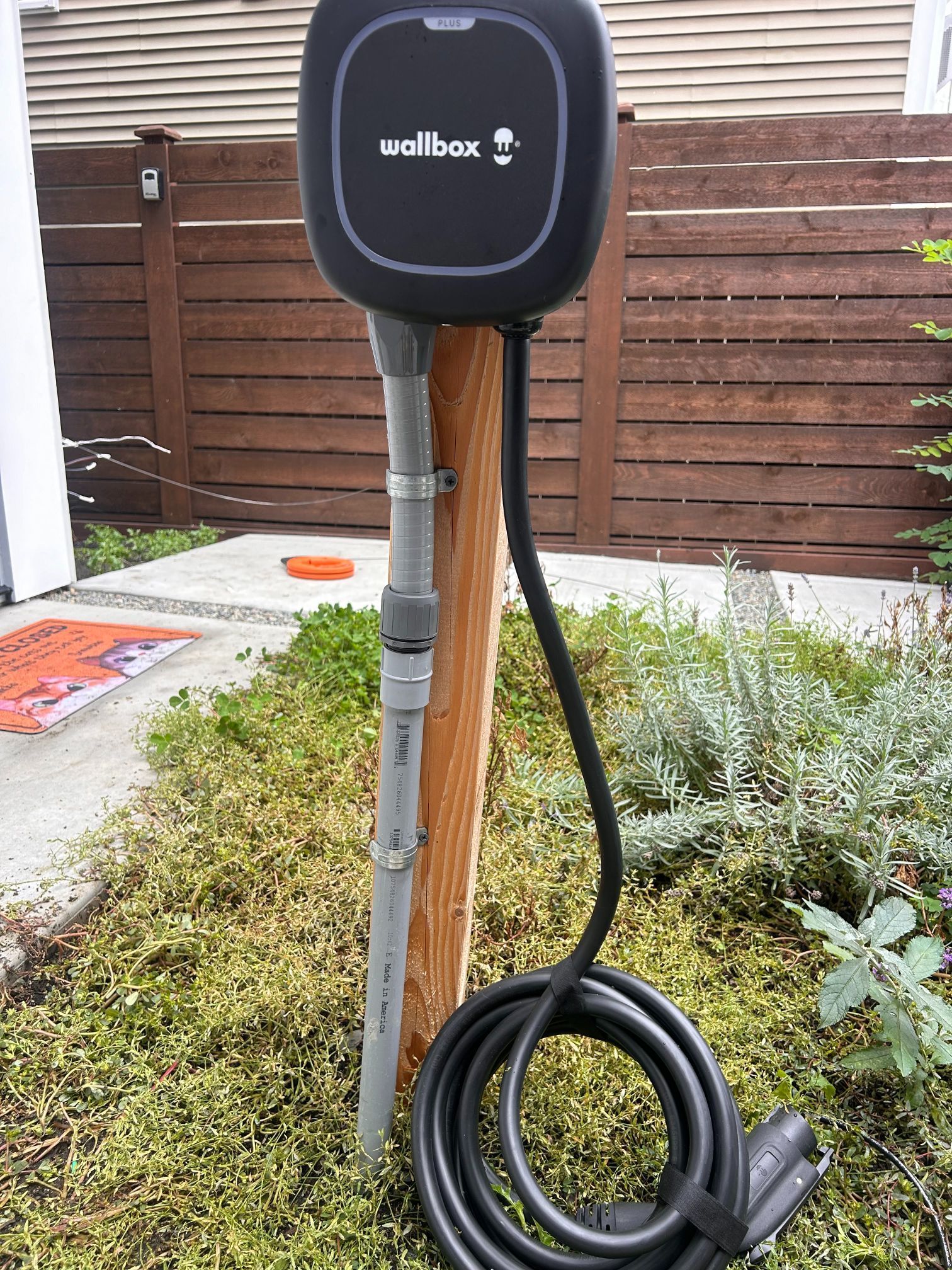 Wallbox electric vehicle charger mounted on a wooden post with coiled charging cable outdoors