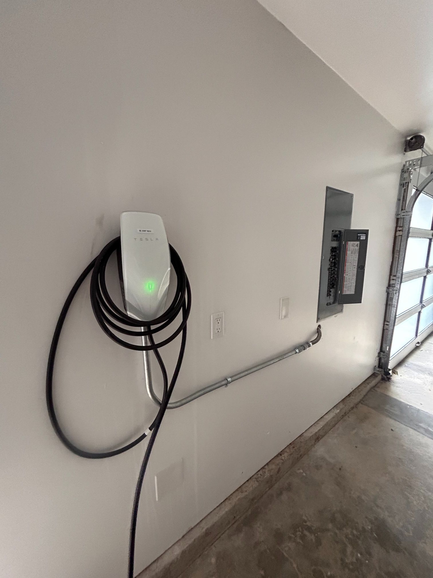 Wall-mounted EV charger with coiled cable in a garage beside an electrical panel