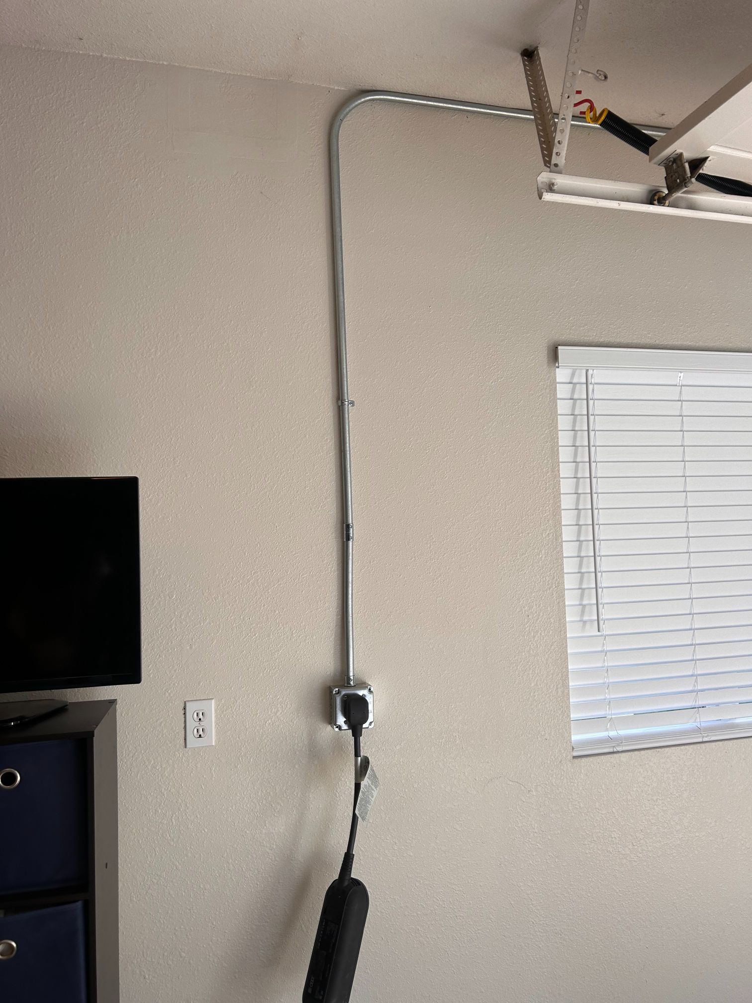 Garage wall with a hanging cable, window blinds, and part of a TV and ceiling track visible.