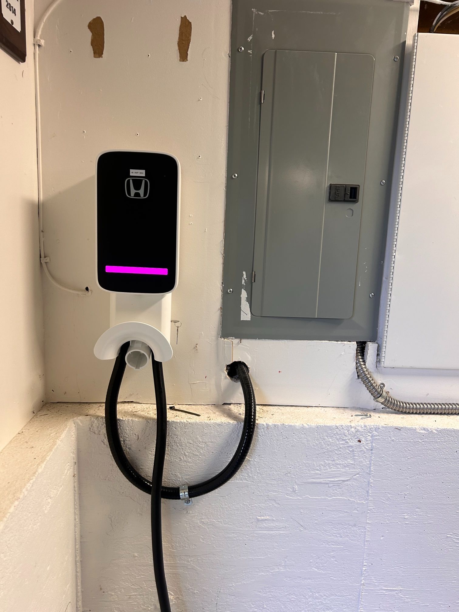 Wall-mounted EV charger with two black cables beside a gray electrical panel.