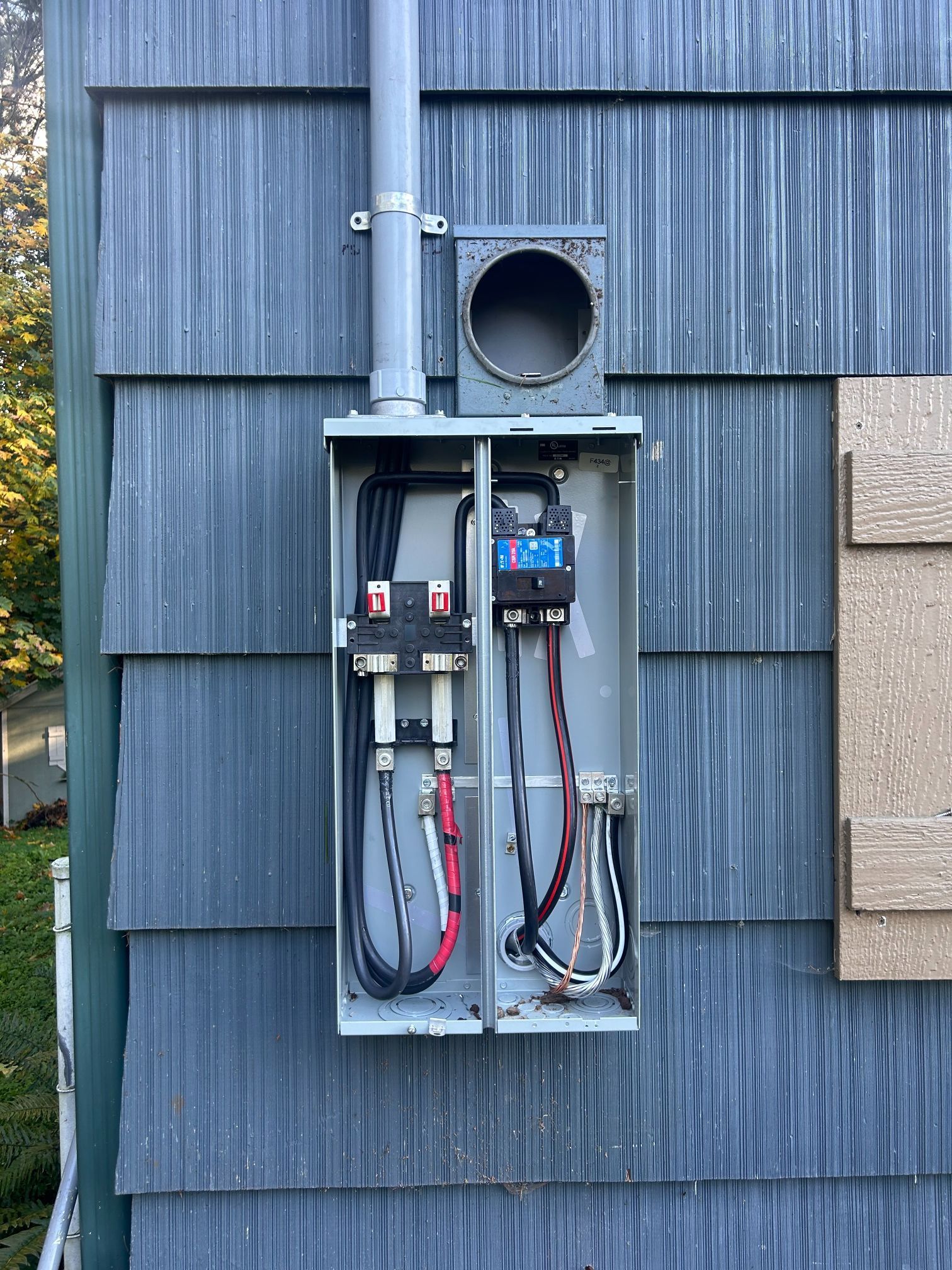 Open electrical meter box with exposed wiring mounted on blue shingle siding