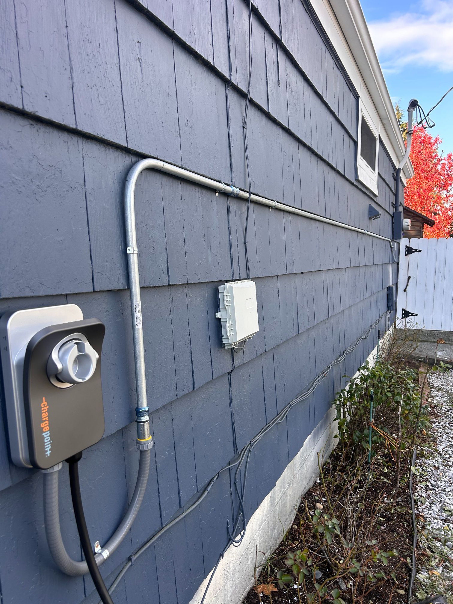 Gray house siding with an electrical meter, conduit, and utility box along the exterior wall