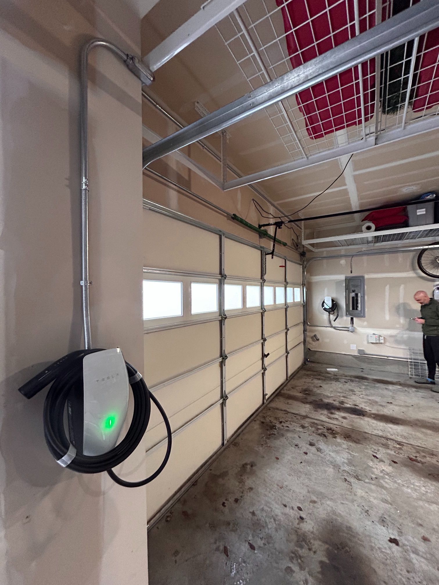 Garage with EV charger mounted on wall, garage door, and a person standing in the background