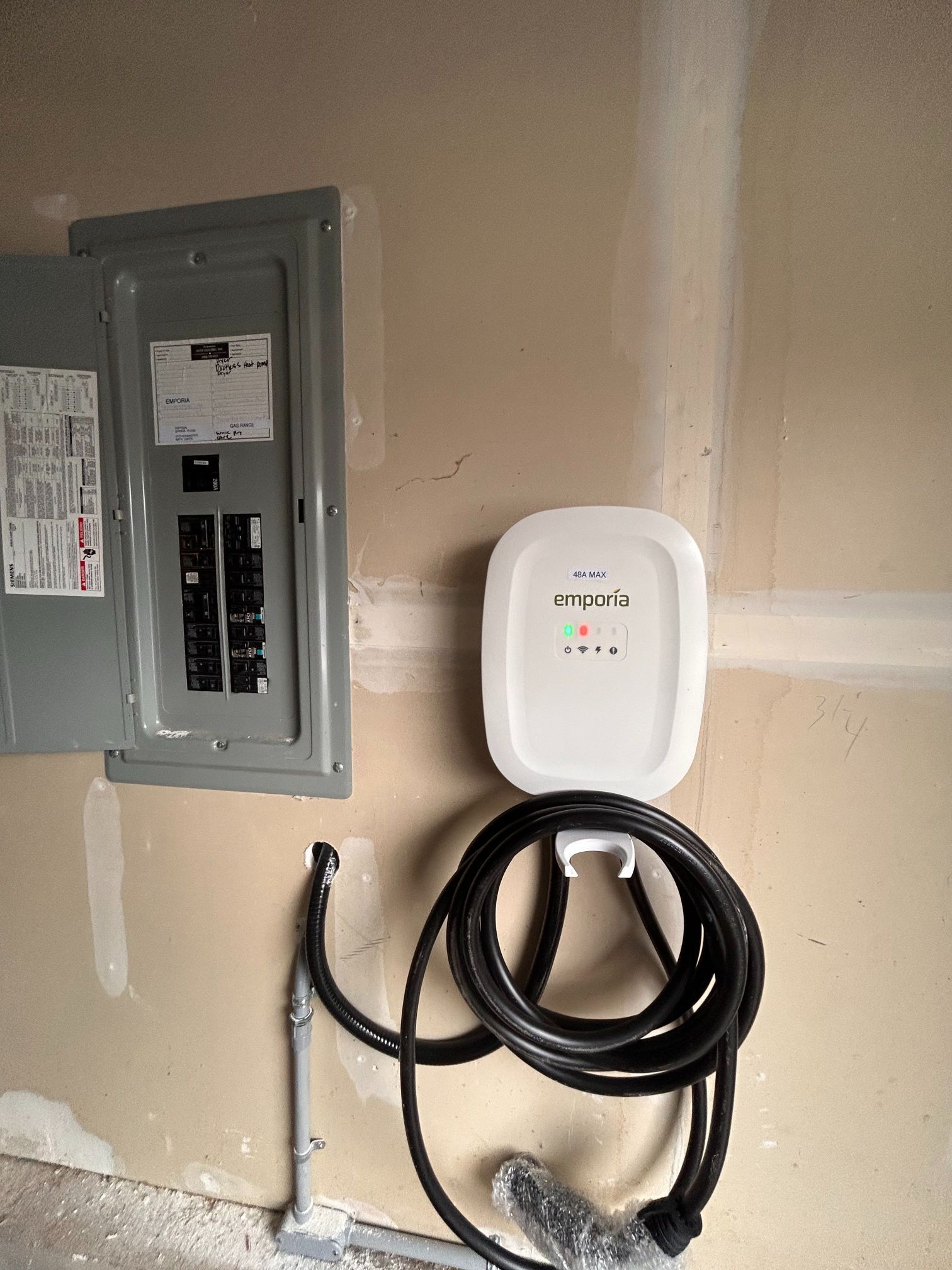 Electrical panel and white wall-mounted device with coiled black cable on a garage wall.