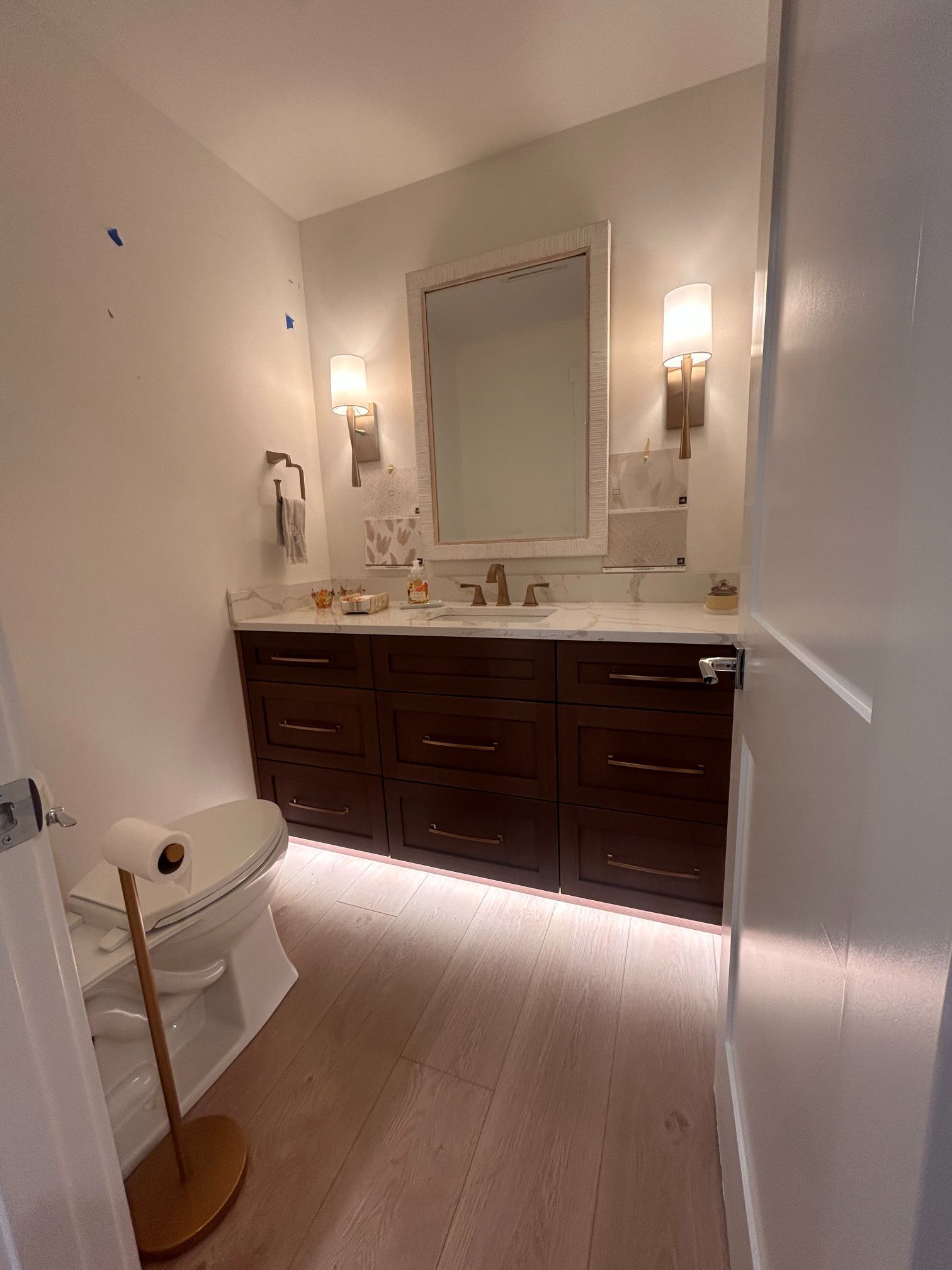 Small powder room with dark wood vanity, large mirror, wall sconces, and a toilet on the left.