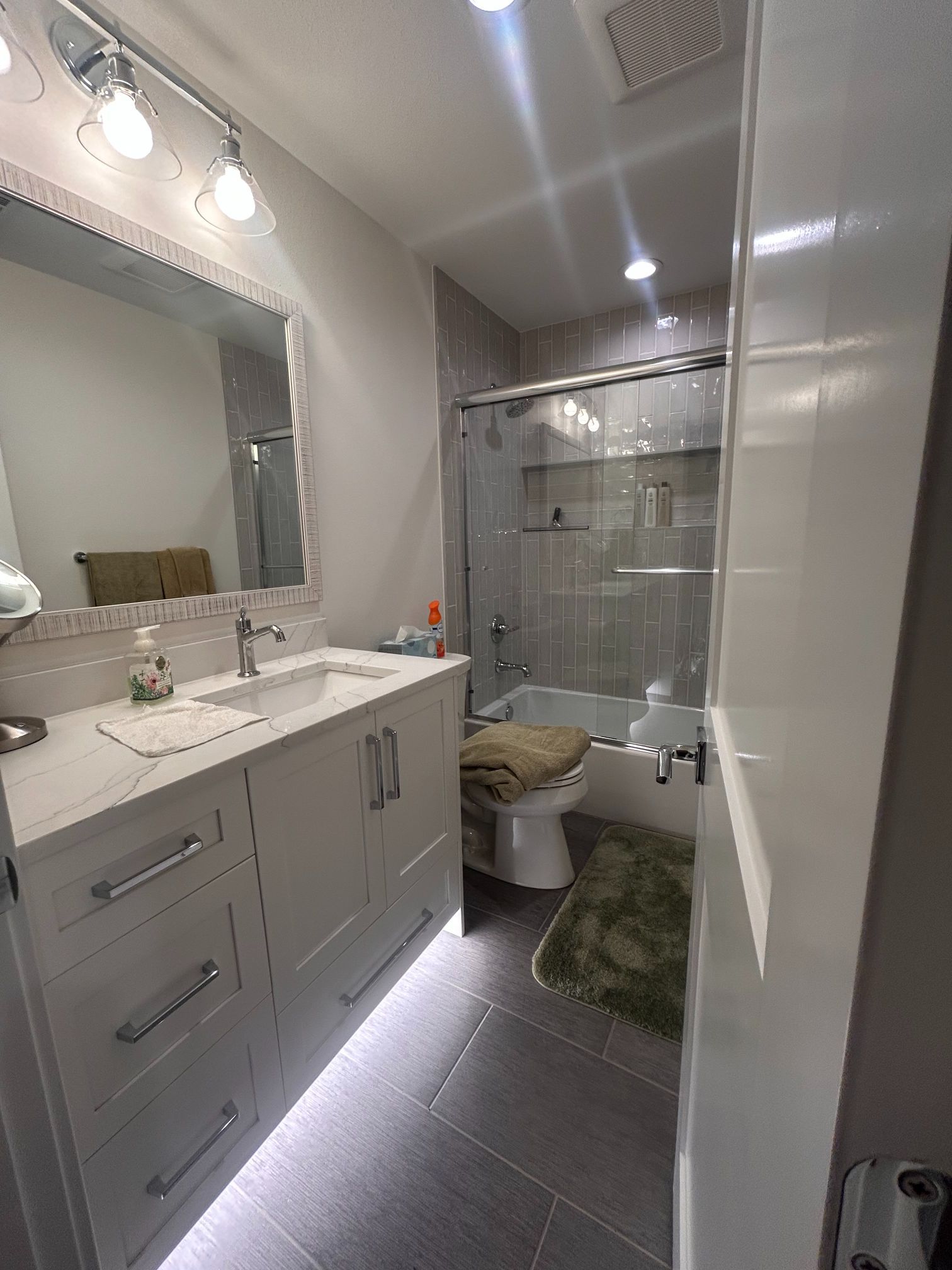 Modern bathroom with vanity, mirror, toilet, glass shower, and green bath mat