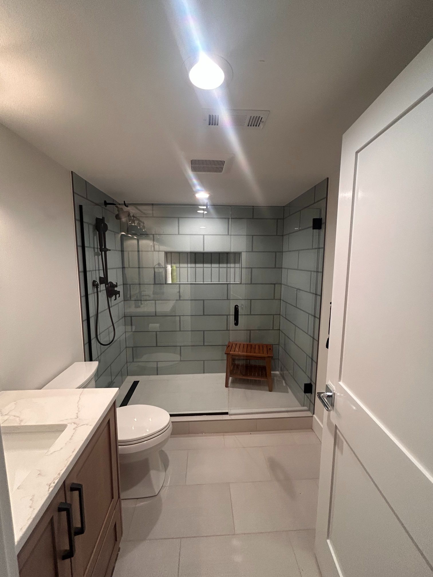 Modern bathroom with walk-in shower, white tile, toilet, sink counter, and bright ceiling light