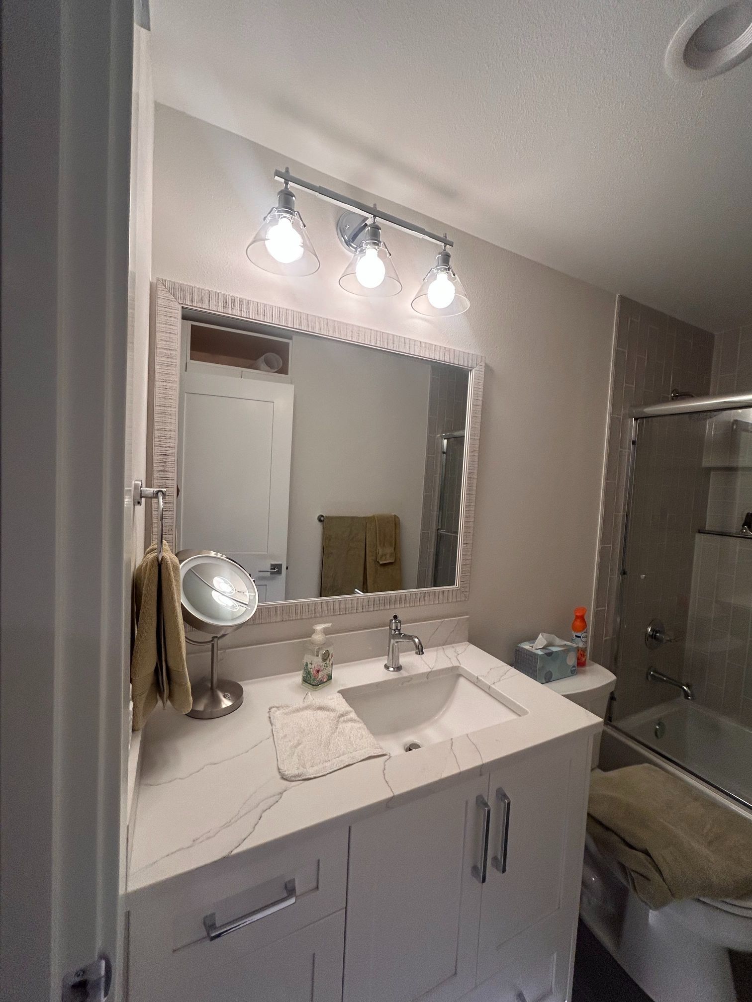 Modern bathroom vanity with lit mirror, sink, and glass shower door.
