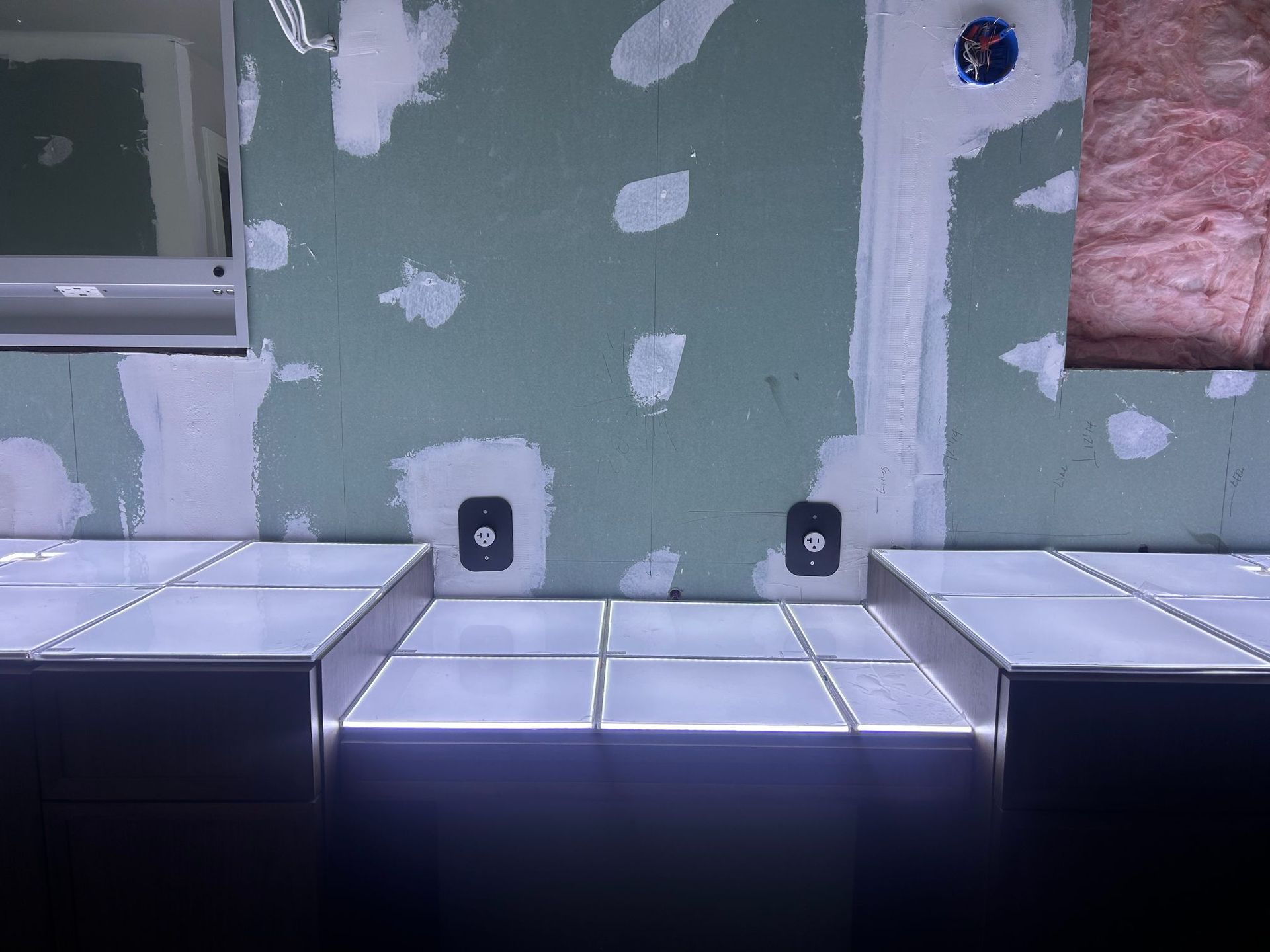 Unfinished room with green drywall, white patches, and a row of metal counters or cabinets along the wall