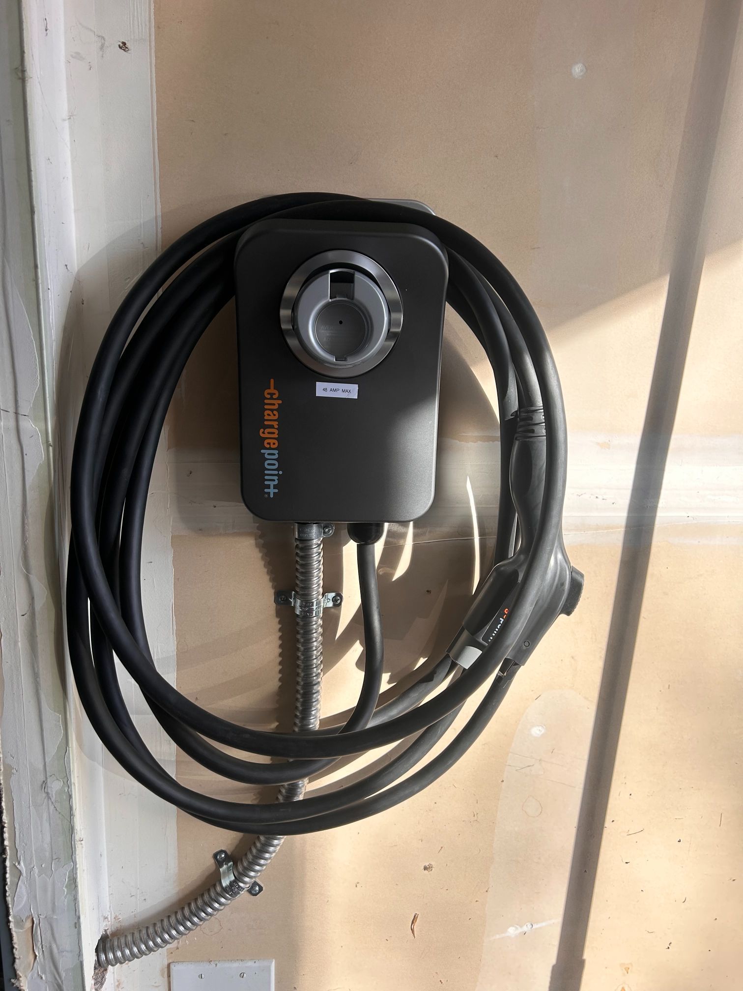 Black EV charging cable coiled around a wall-mounted charger box indoors.