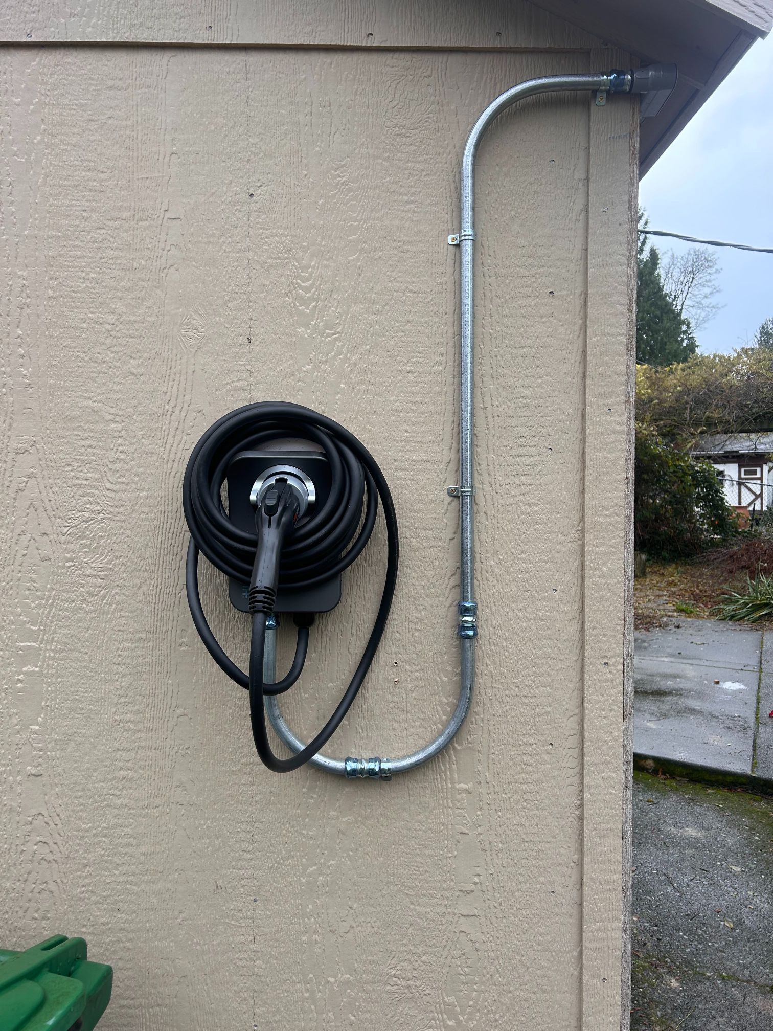 Black wall-mounted EV charging cable reel on a beige exterior wall with conduit piping