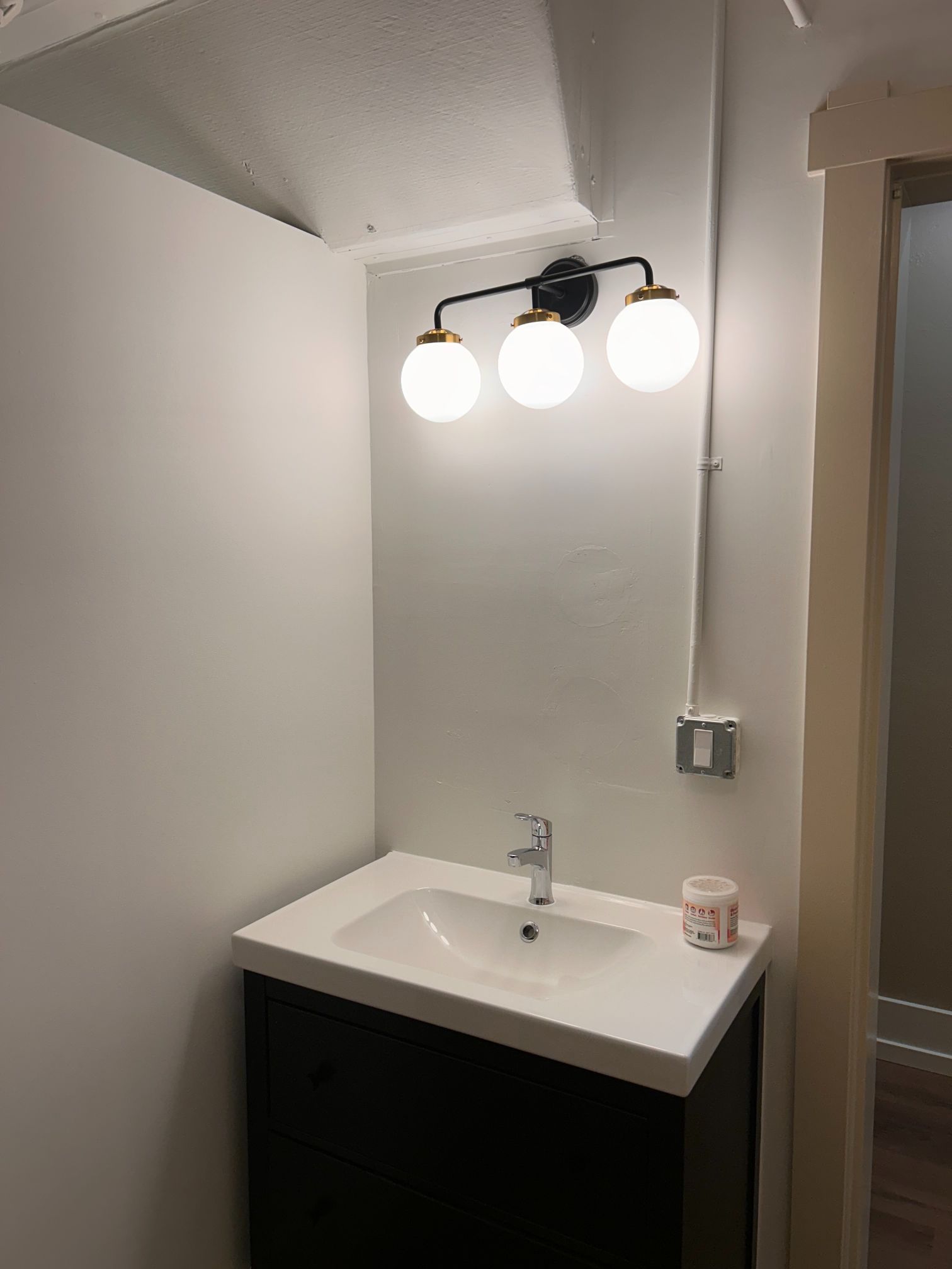 Small bathroom vanity with mirror, three globe lights, white sink, and dark cabinet.