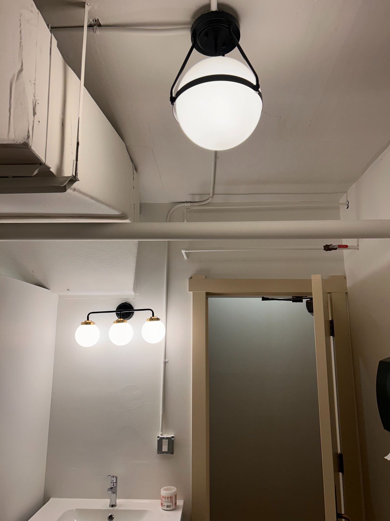Small bathroom with white walls, a frosted door, and two lit ceiling fixtures.