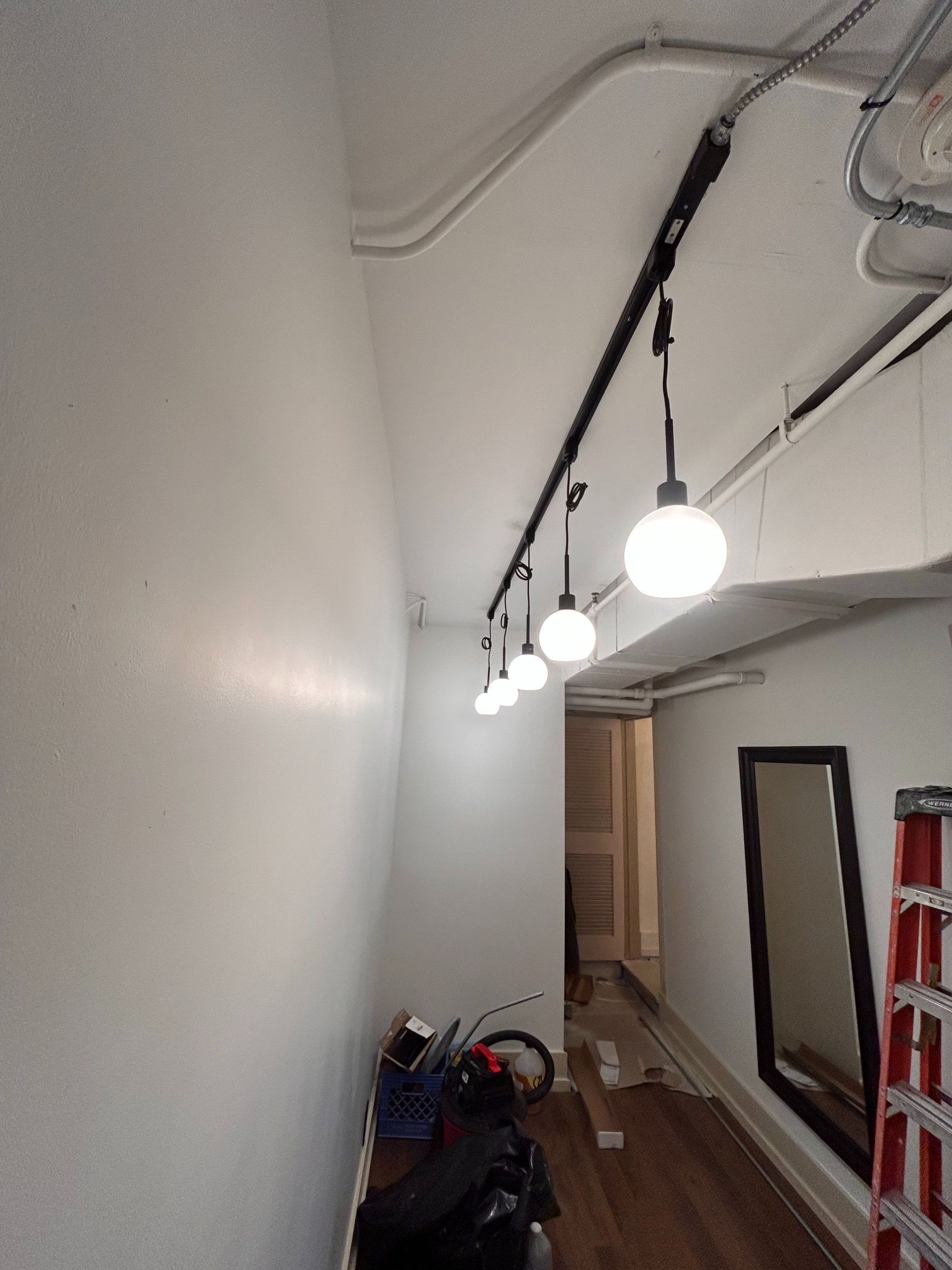 Narrow hallway with exposed ceiling lights, wood floor, and a red ladder leaning against the wall.