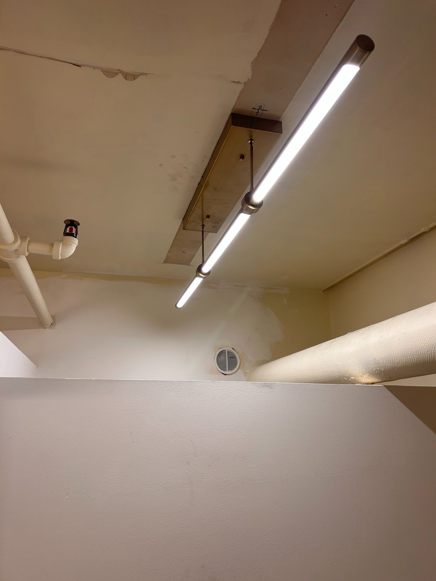 Ceiling with fluorescent lights and exposed pipes above a partition wall in an indoor corridor
