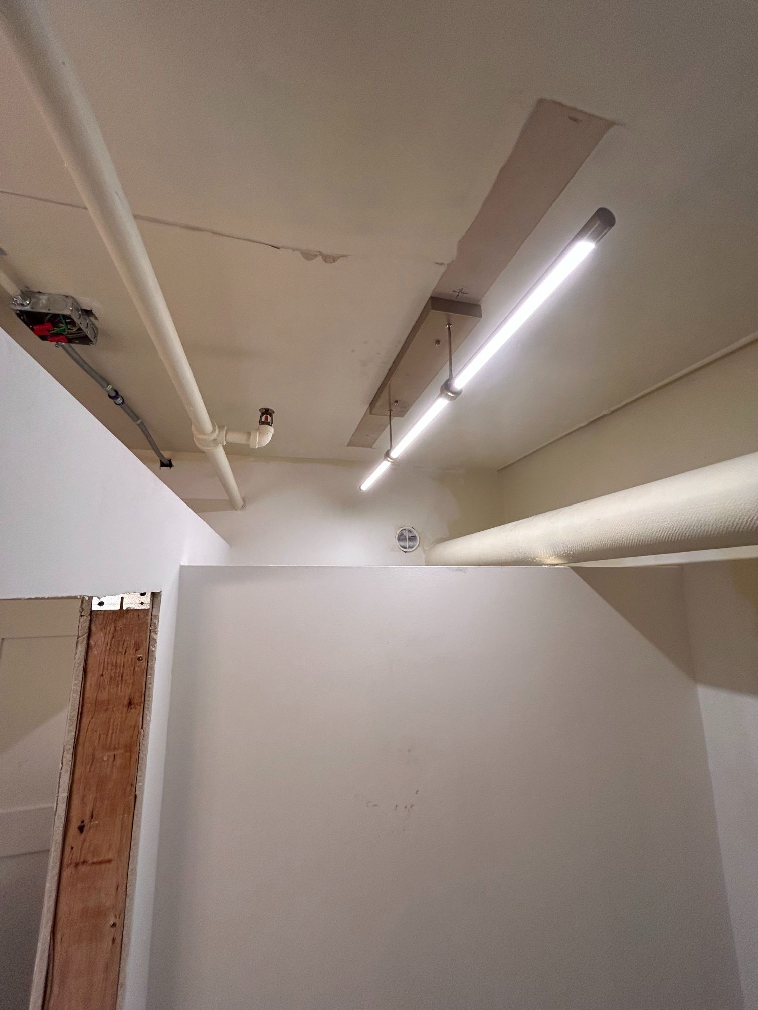 Empty white hallway with exposed ceiling pipes and bright fluorescent lights