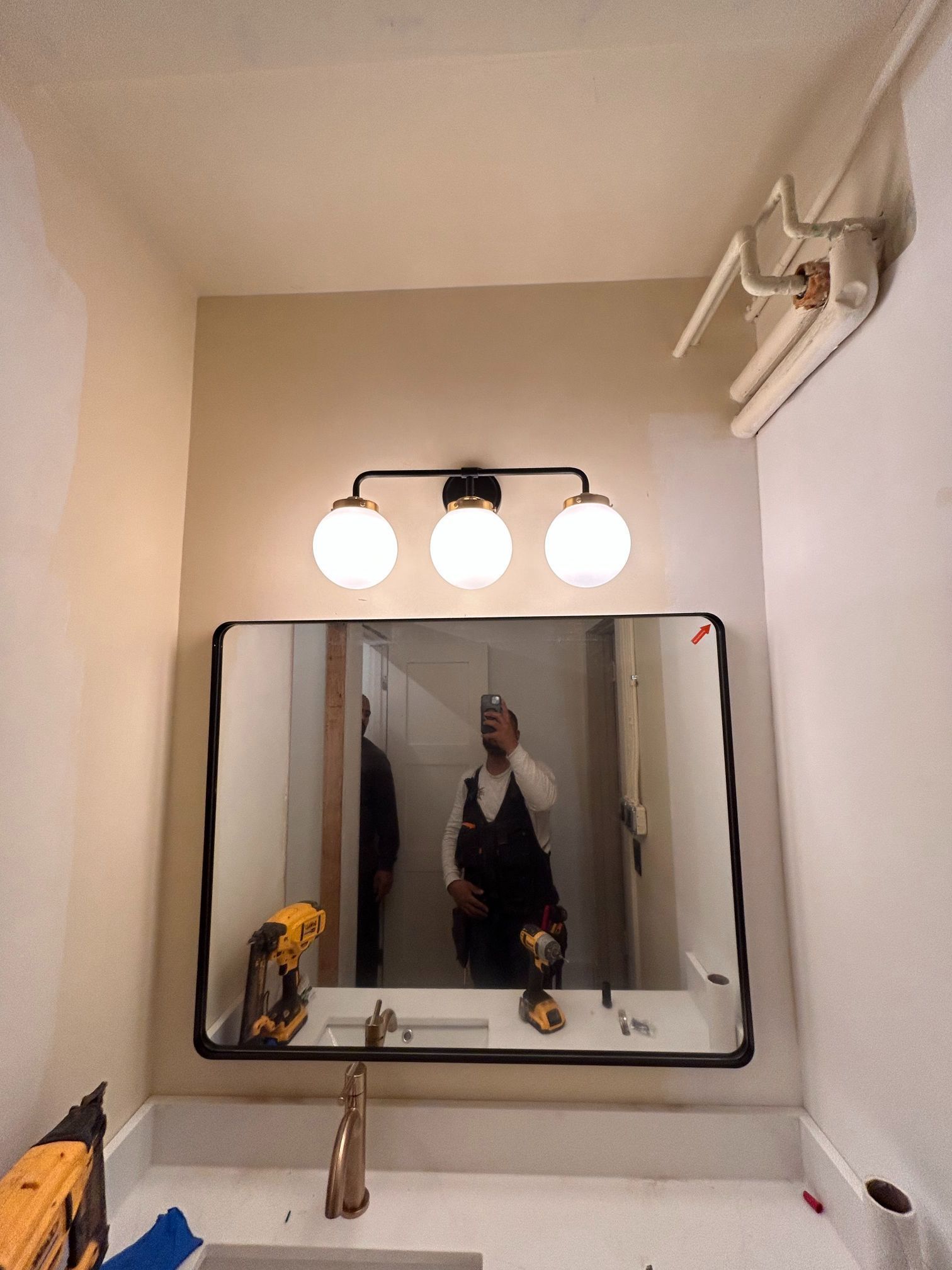 Bathroom mirror above sink with three globe lights and a person reflected in the mirror.