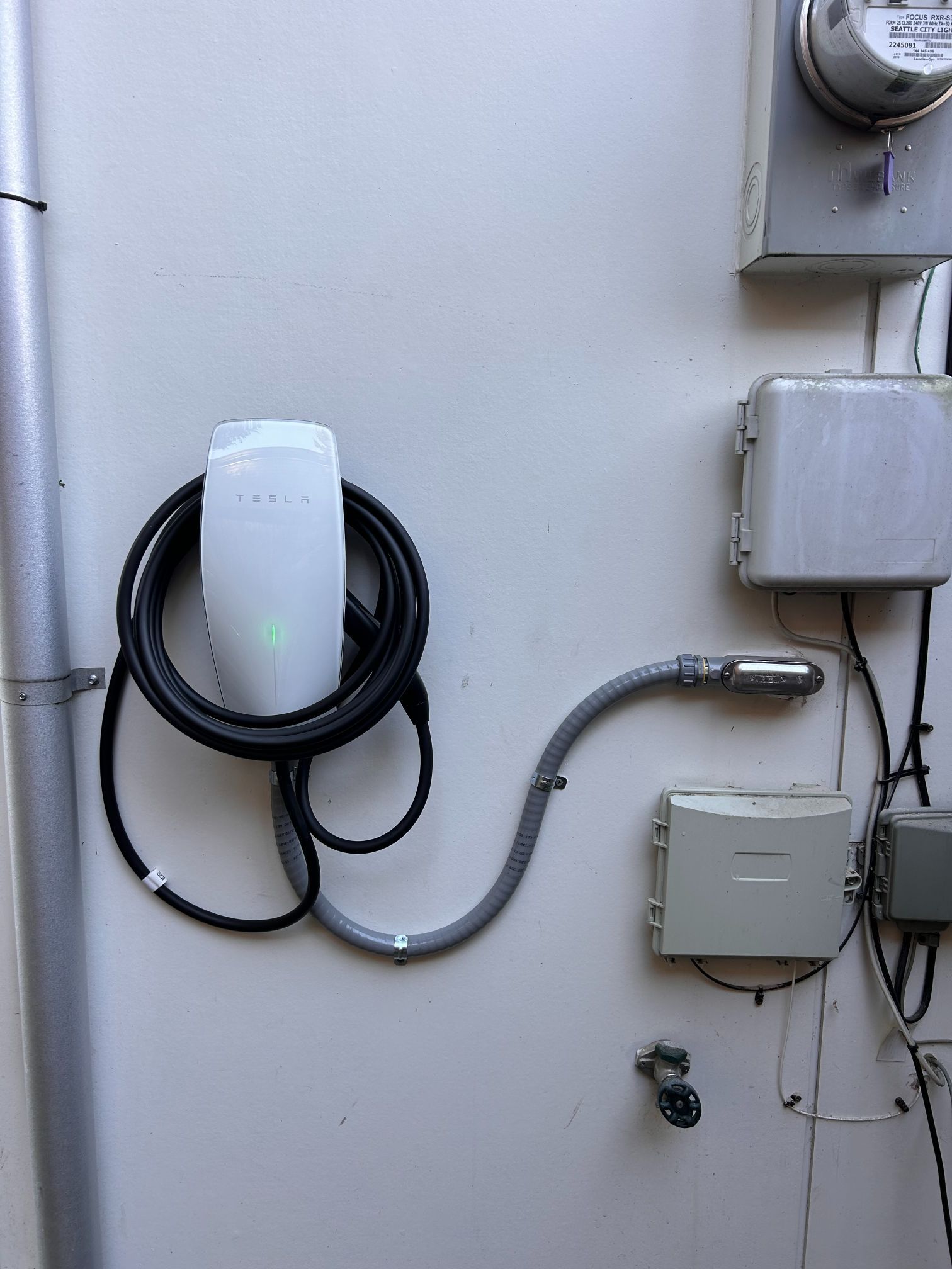 Wall-mounted utility equipment with coiled black cable, white boxes, and conduit on a gray exterior wall