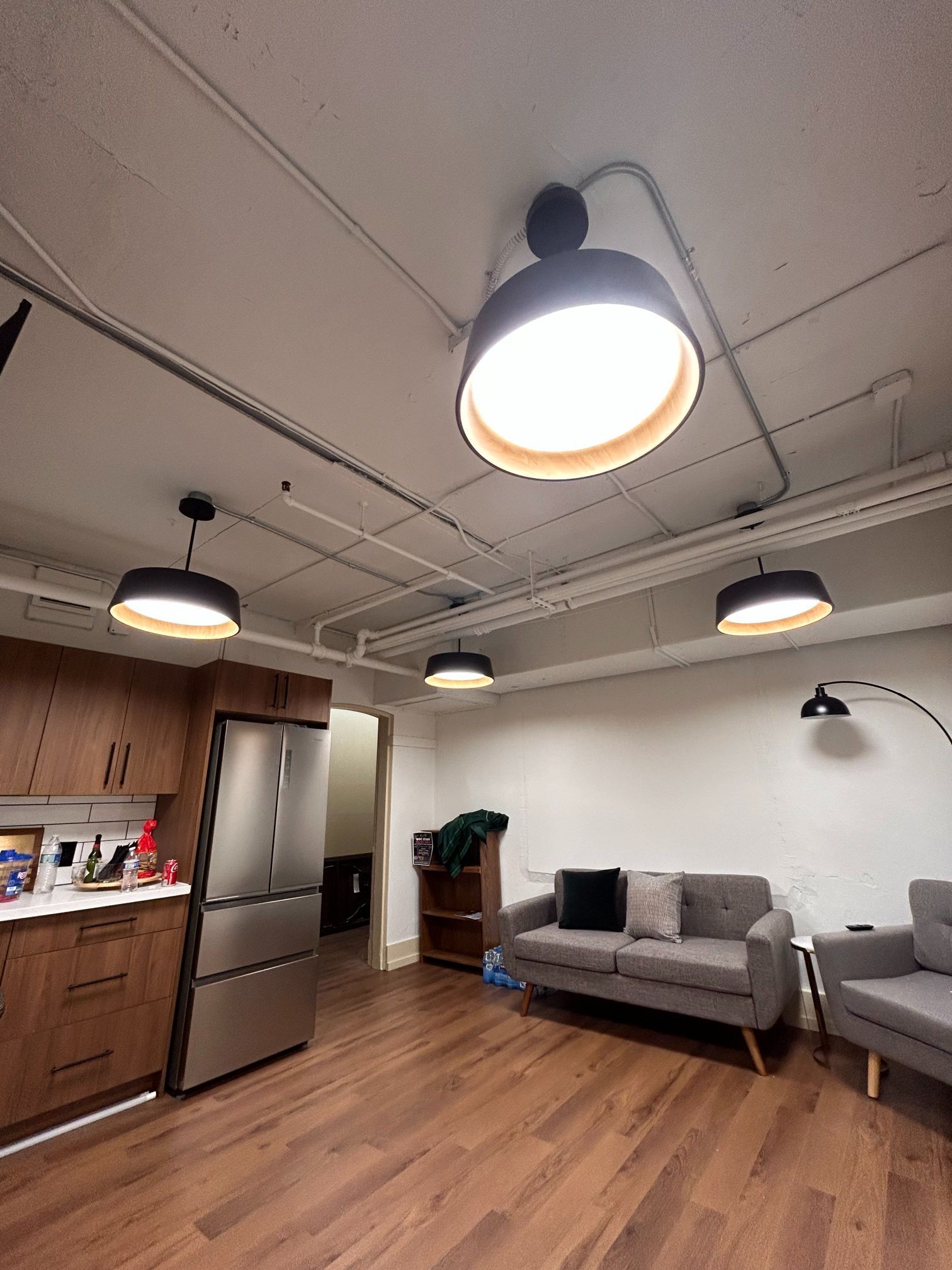 Modern apartment living room with kitchen, gray sofa, wood floors, and hanging pendant lights