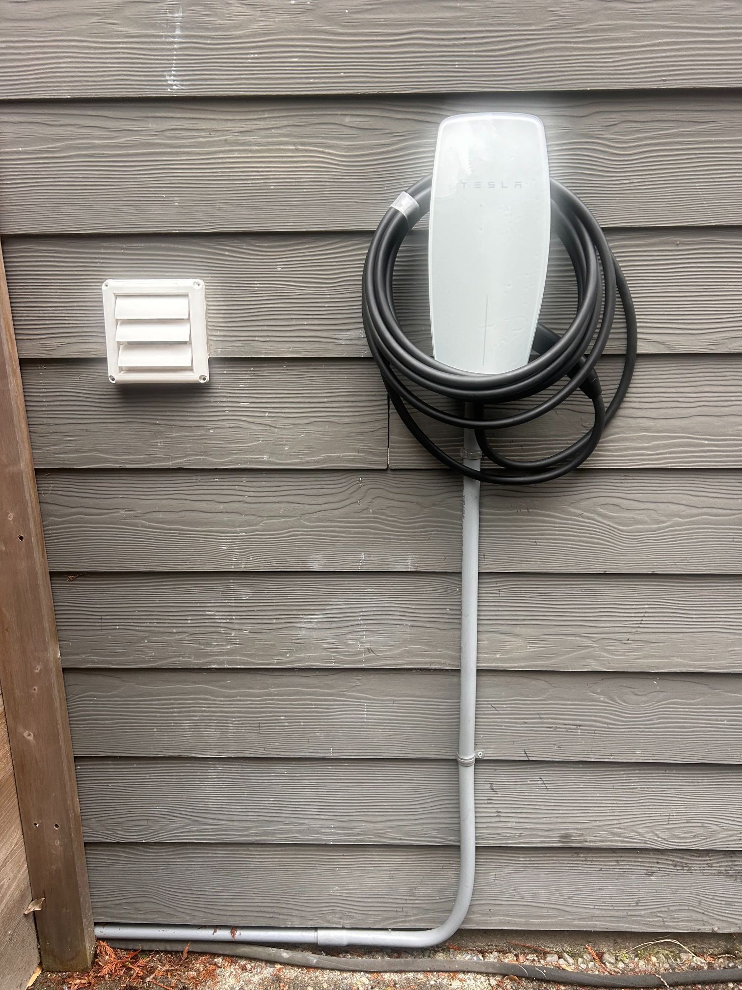 Wall-mounted EV charging unit with coiled black cable on gray house siding