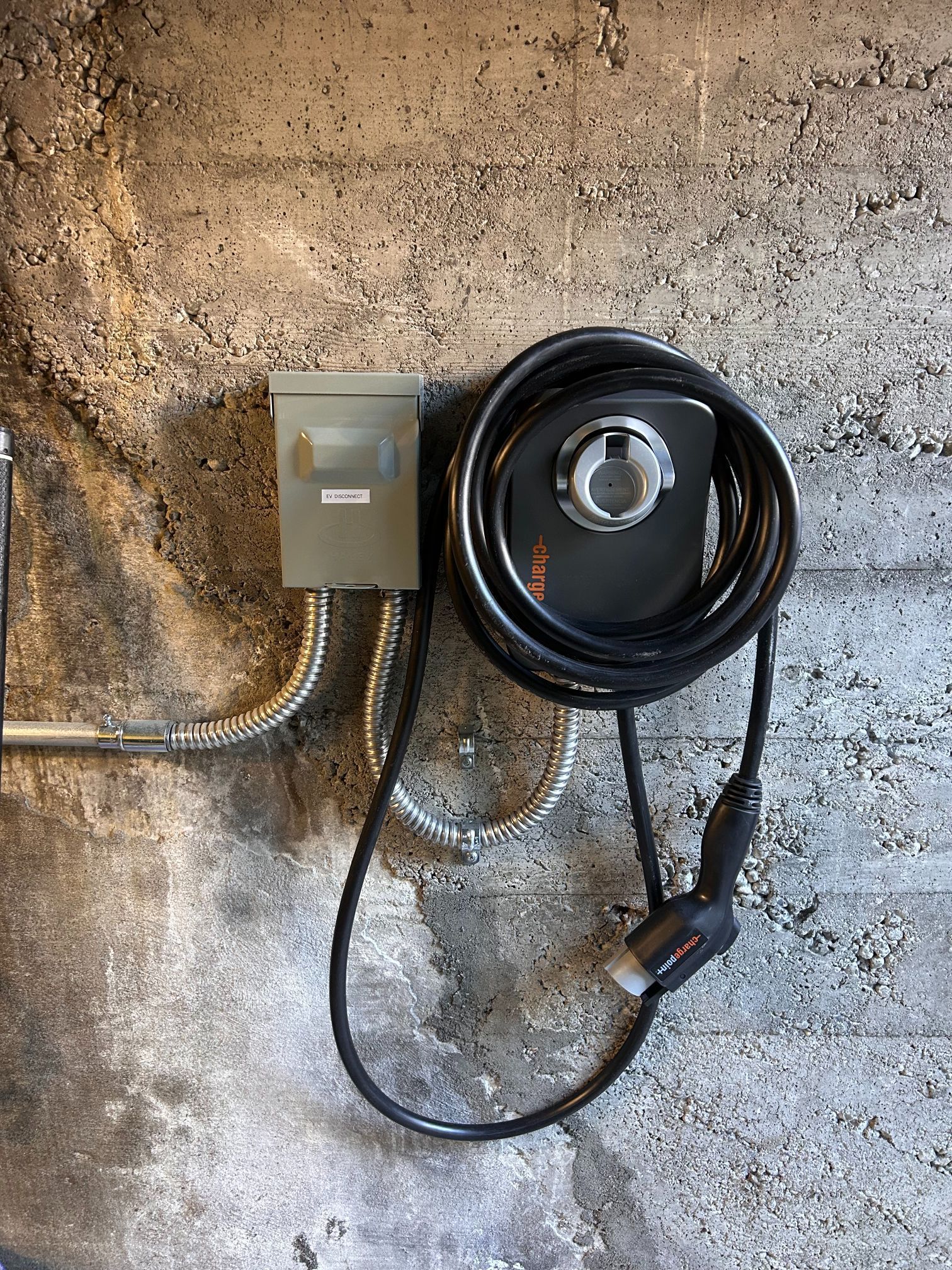 Wall-mounted electrical box and coiled black cable on a rough concrete wall.