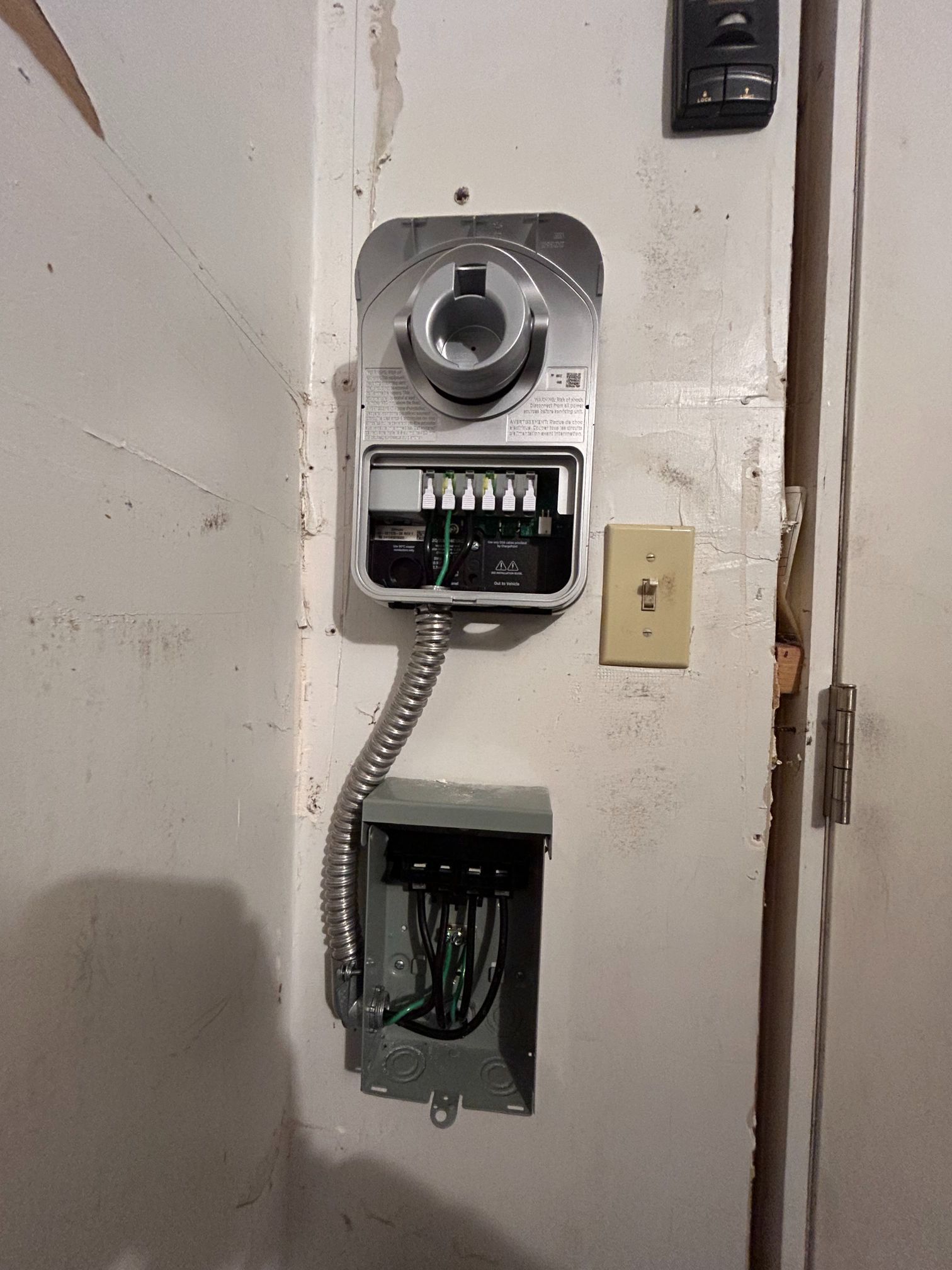 Wall-mounted electrical panel and open junction box on a white wall, with exposed wiring and conduit.