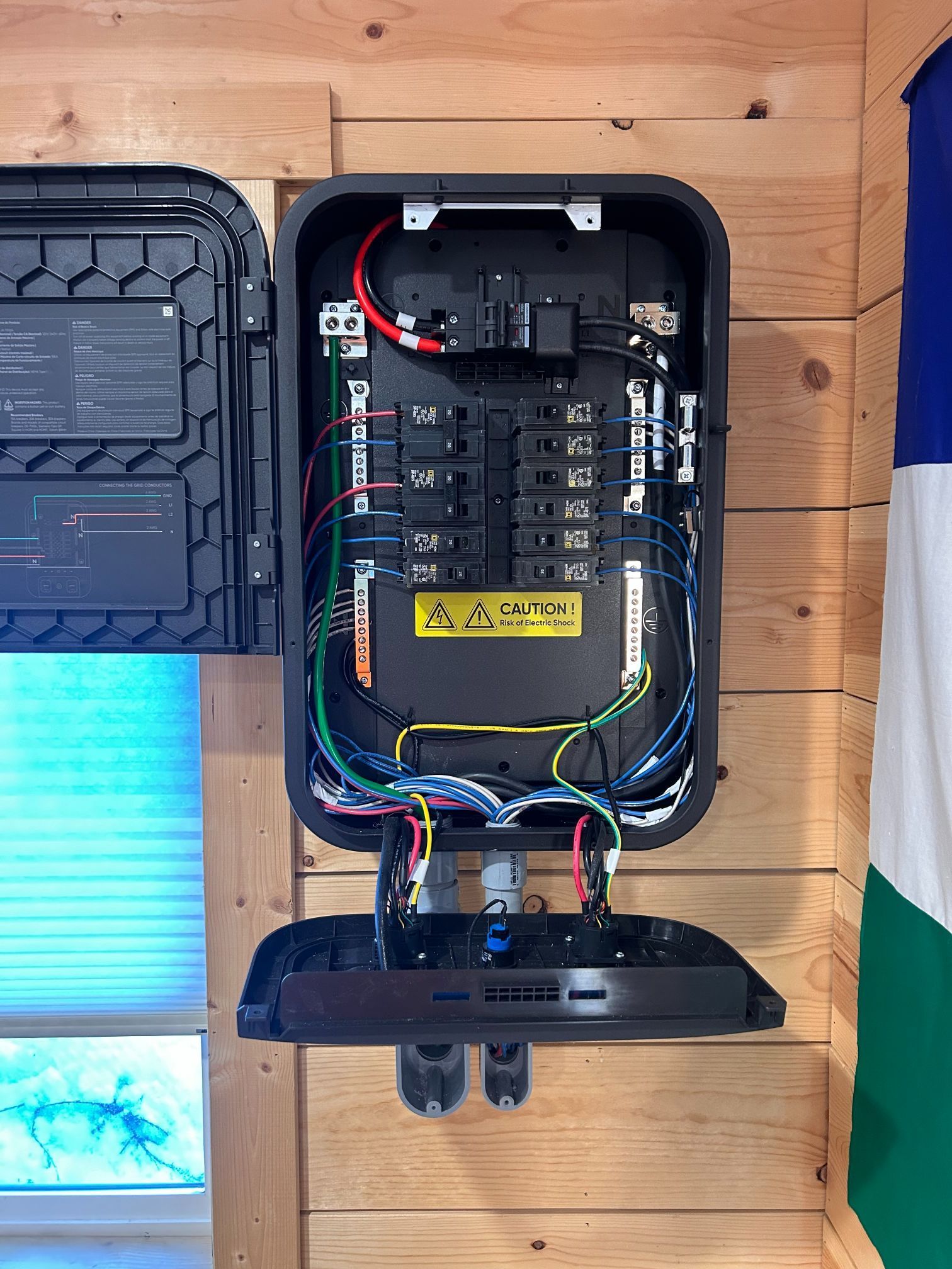 Open electrical breaker panel mounted on a wooden wall, with wiring and a hinged cover.