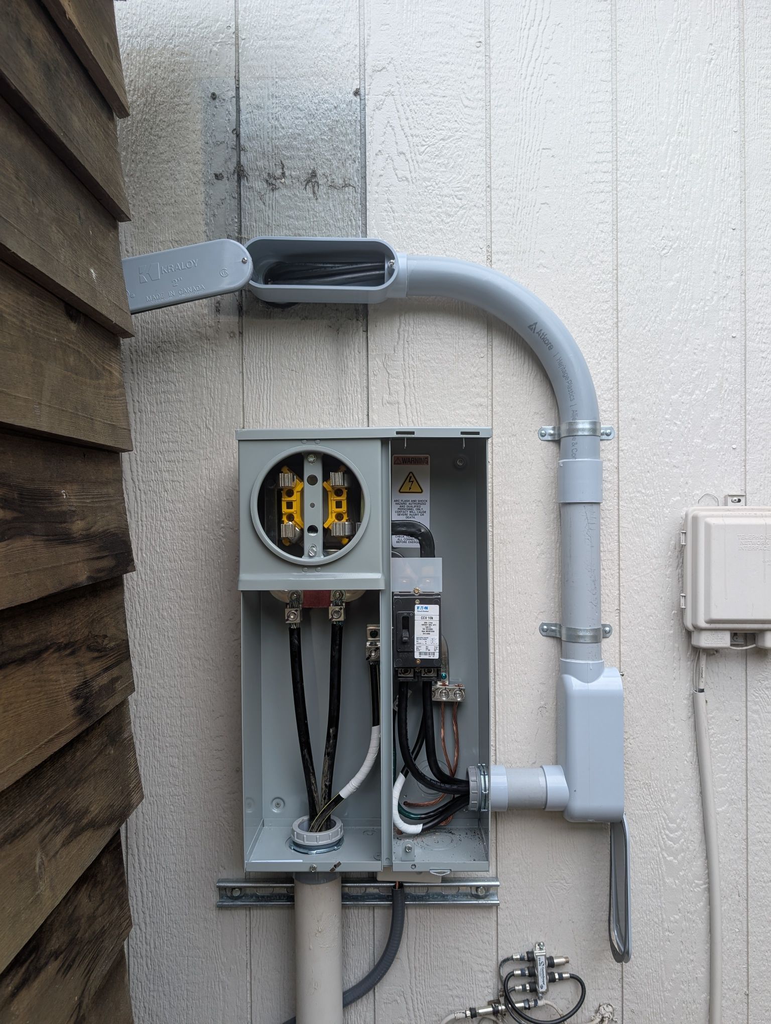 Open electrical meter and conduit mounted on an exterior wall beside a building.