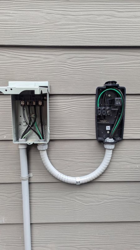Electrical wiring and meter boxes mounted on beige house siding, connected by a white conduit.