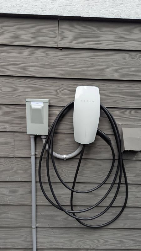 Wall-mounted EV charging unit and electrical box on gray siding with coiled black cable