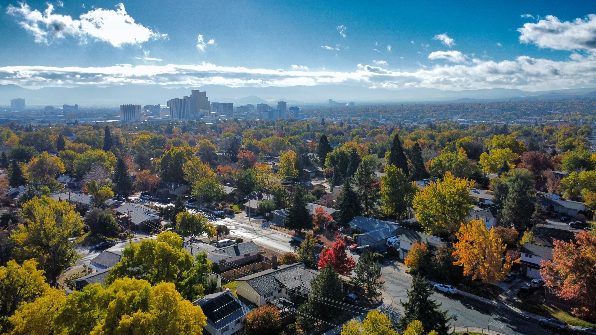 Aerial view of a city with fall foliage, buildings in the distance, and blue sky. Aerial view of a city with fall foliage, buildings in the distance, and blue sky.