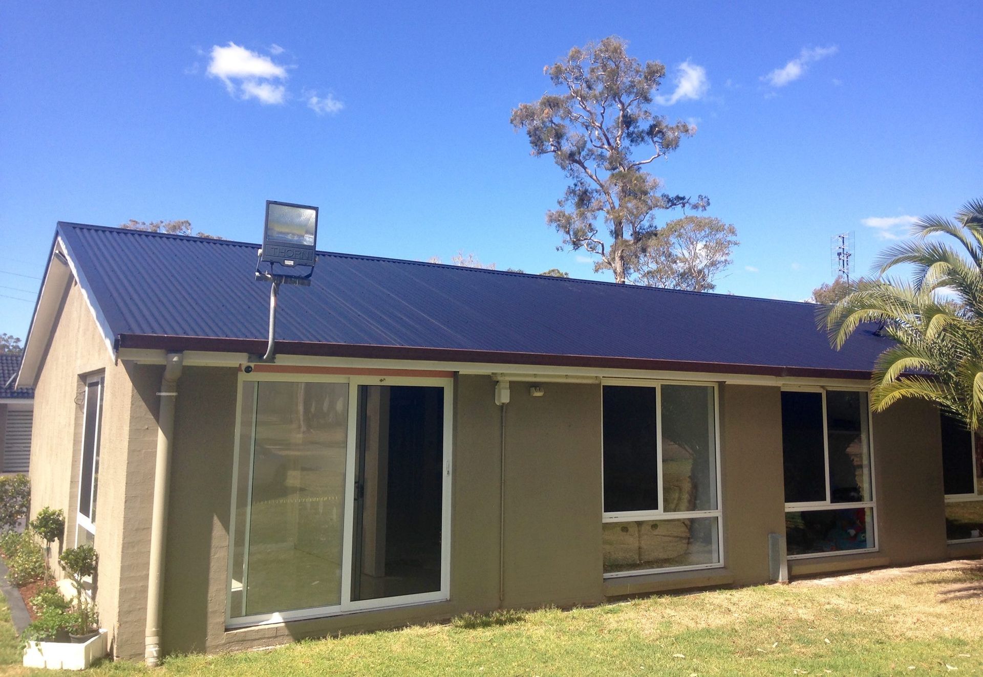 A Small House With A Black Roof Is Sitting On Top Of A Lush Green Field — In-Time Roofing In Newcastle, NSW