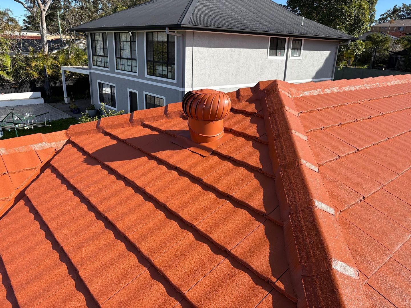 Red tiled roof with a vent, viewed from above; house exterior in the background — In-Time Roofing In Newcastle, NSW