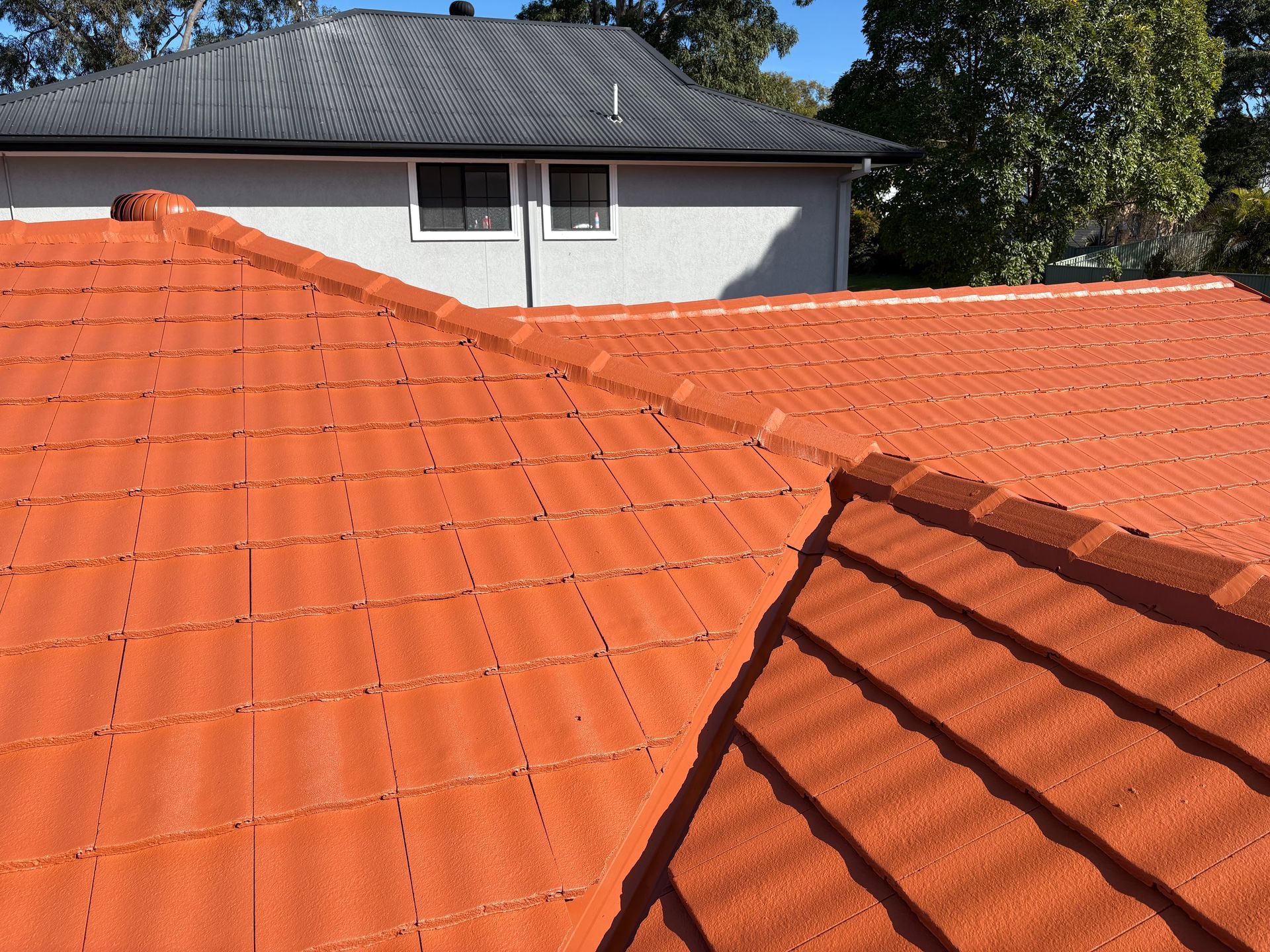 Orange tile roof with a house and trees in the background, seen from above — In-Time Roofing In Newcastle, NSW
