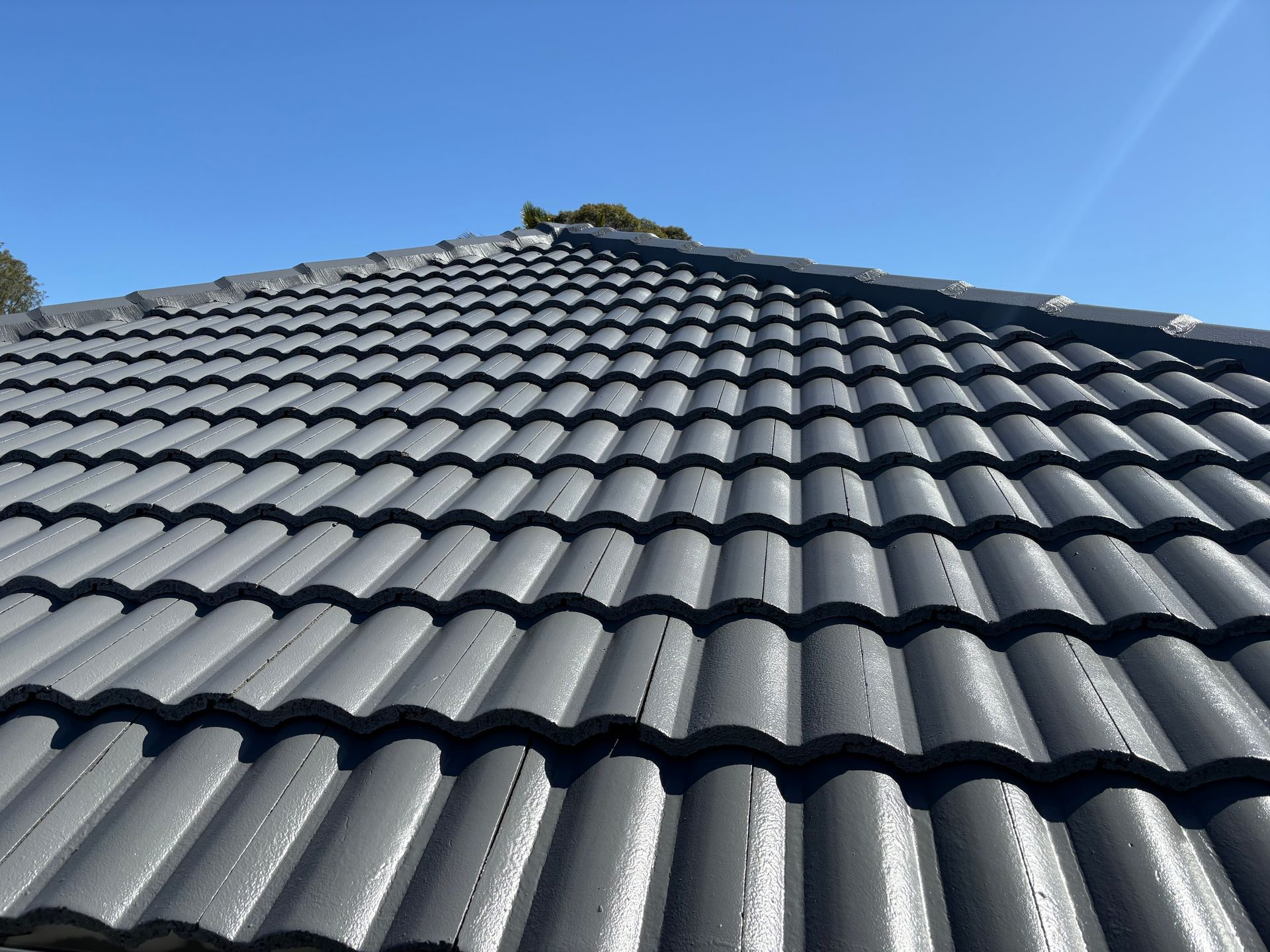 Close-up of a dark gray tiled roof against a blue sky, viewed upward — In-Time Roofing In Newcastle, NSW